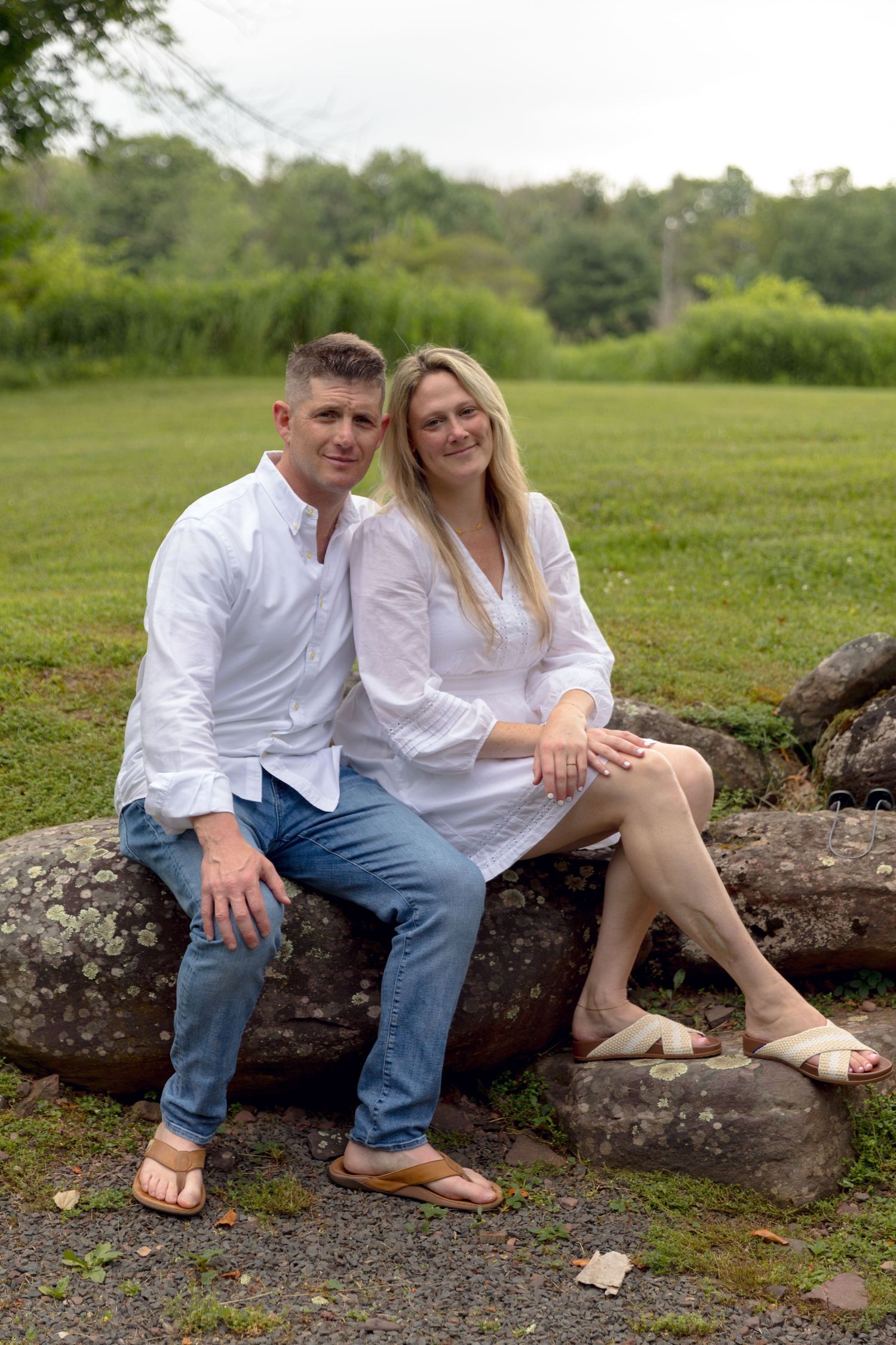 A couple sits together on a stone wall outdoors wearing matching white shirts.