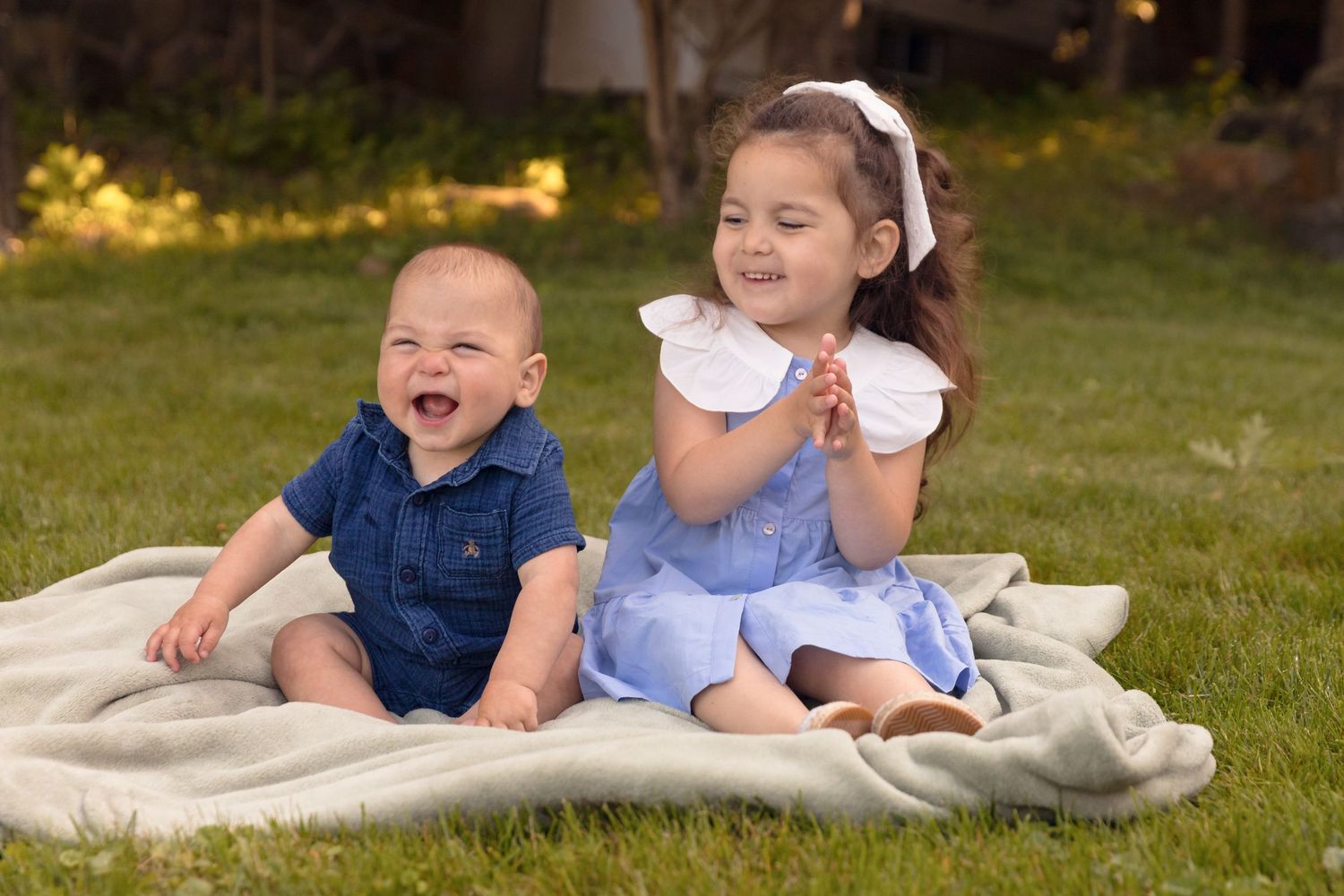 Children sitting together on white blanket during outdoor photo session.