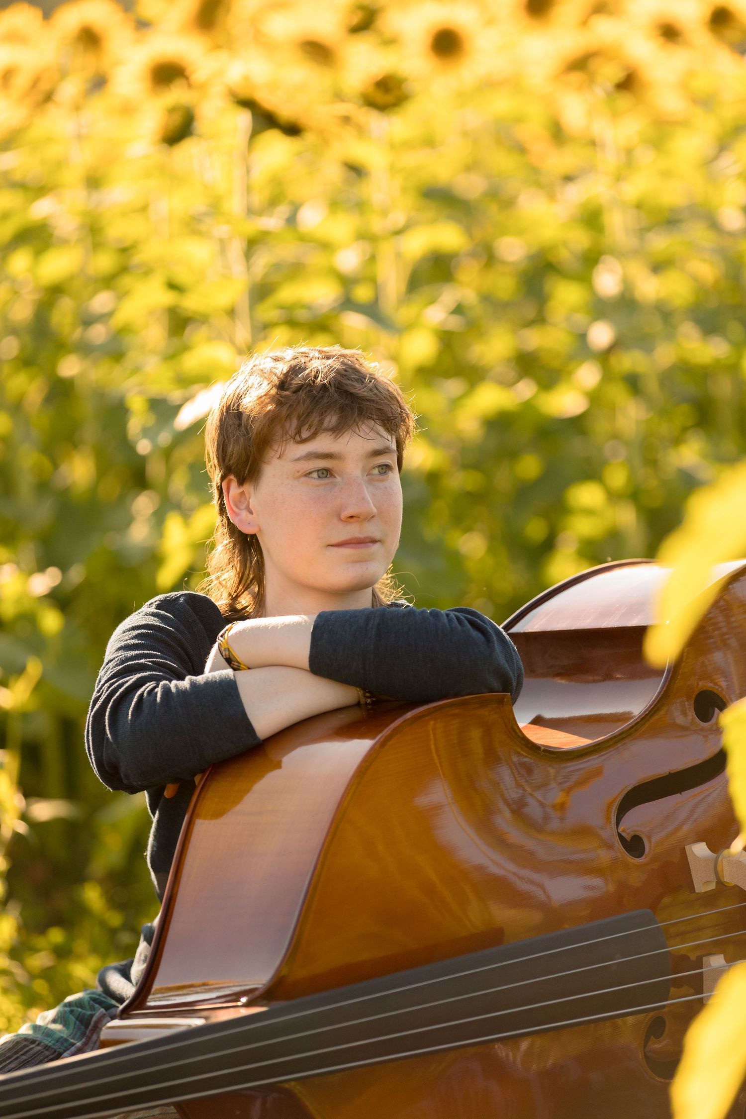 Musician resting on upright bass with sunflowers glowing in background.