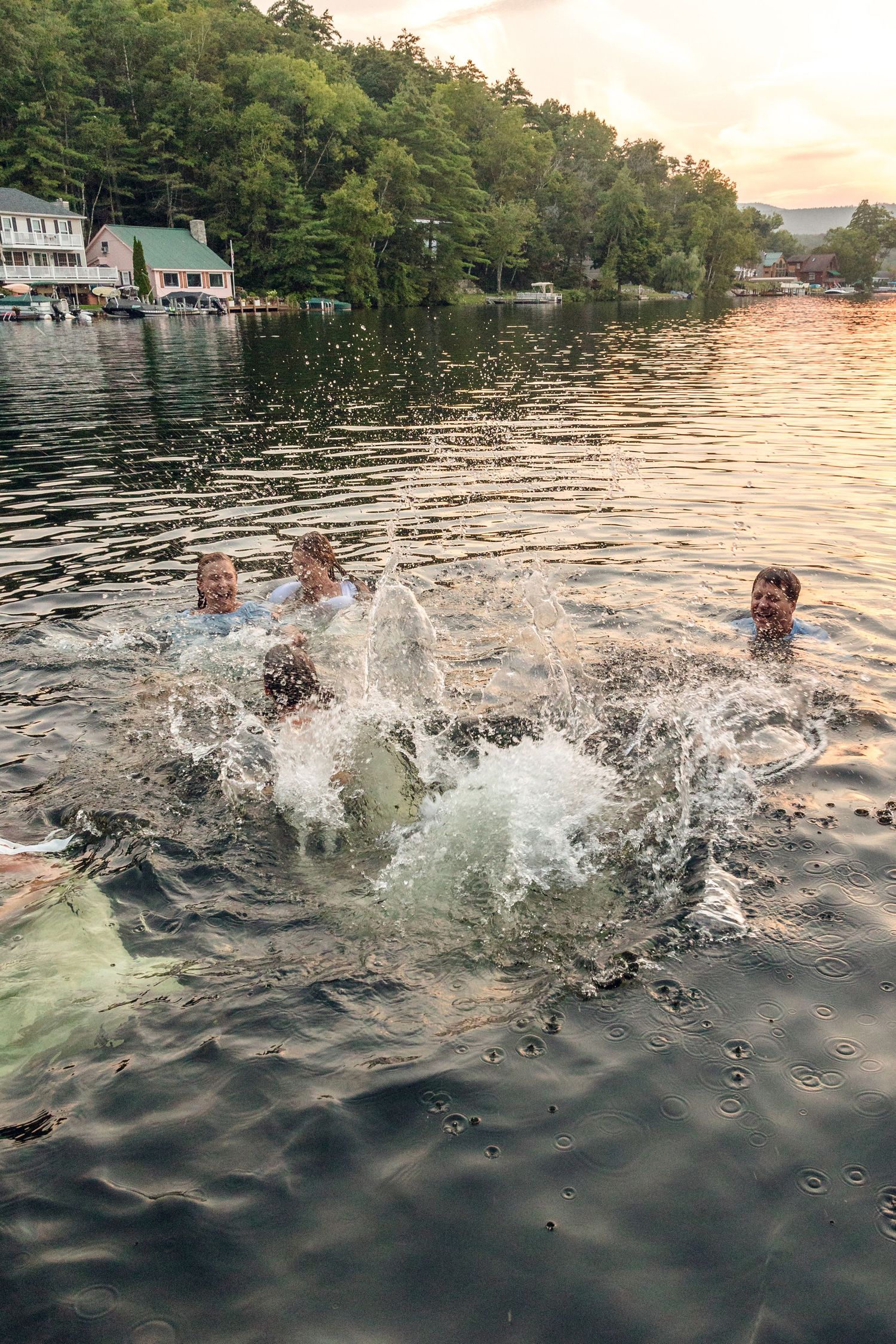 Splashing water sequence captured during sunset on a lake with lakeside homes visible.