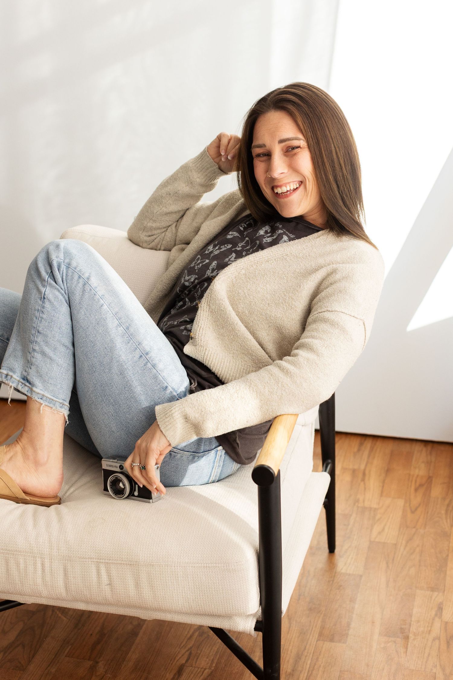 Person relaxing on beige armchair wearing cozy sweater and jeans in bright minimalist interior.
