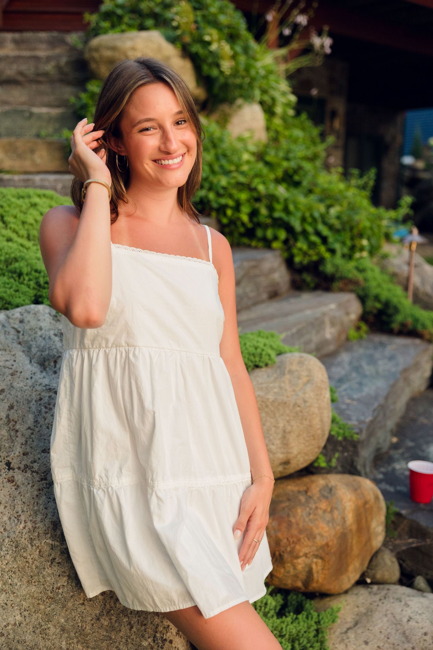 Person in a white summer dress poses on rocky lakeside terrain during sunset.