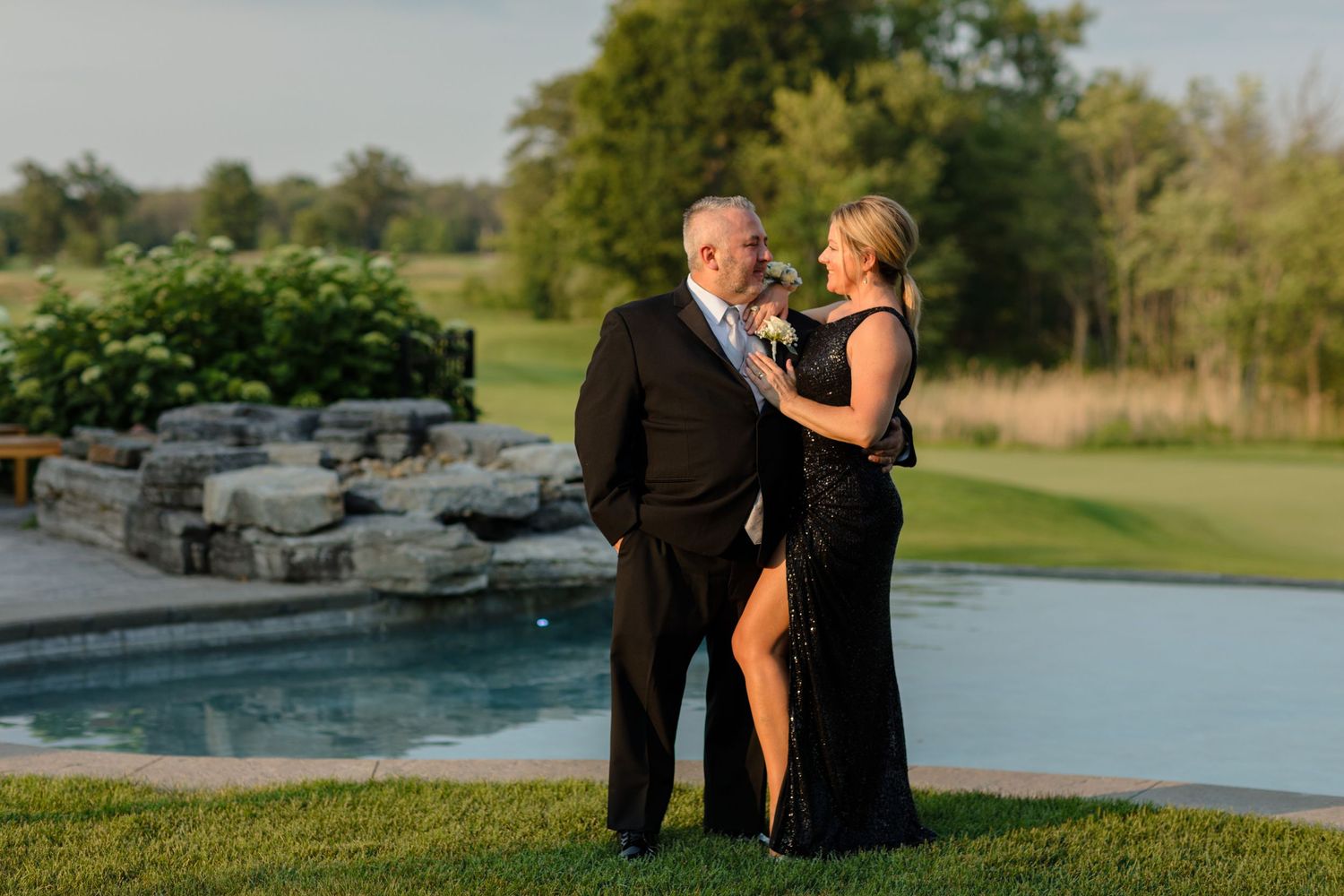 Elegant couple poses by an infinity pool at sunset in formal attire.