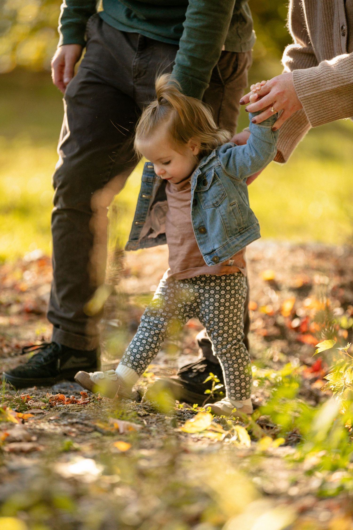 Close-up of child's feet in polka dot pants walking through fallen leaves.