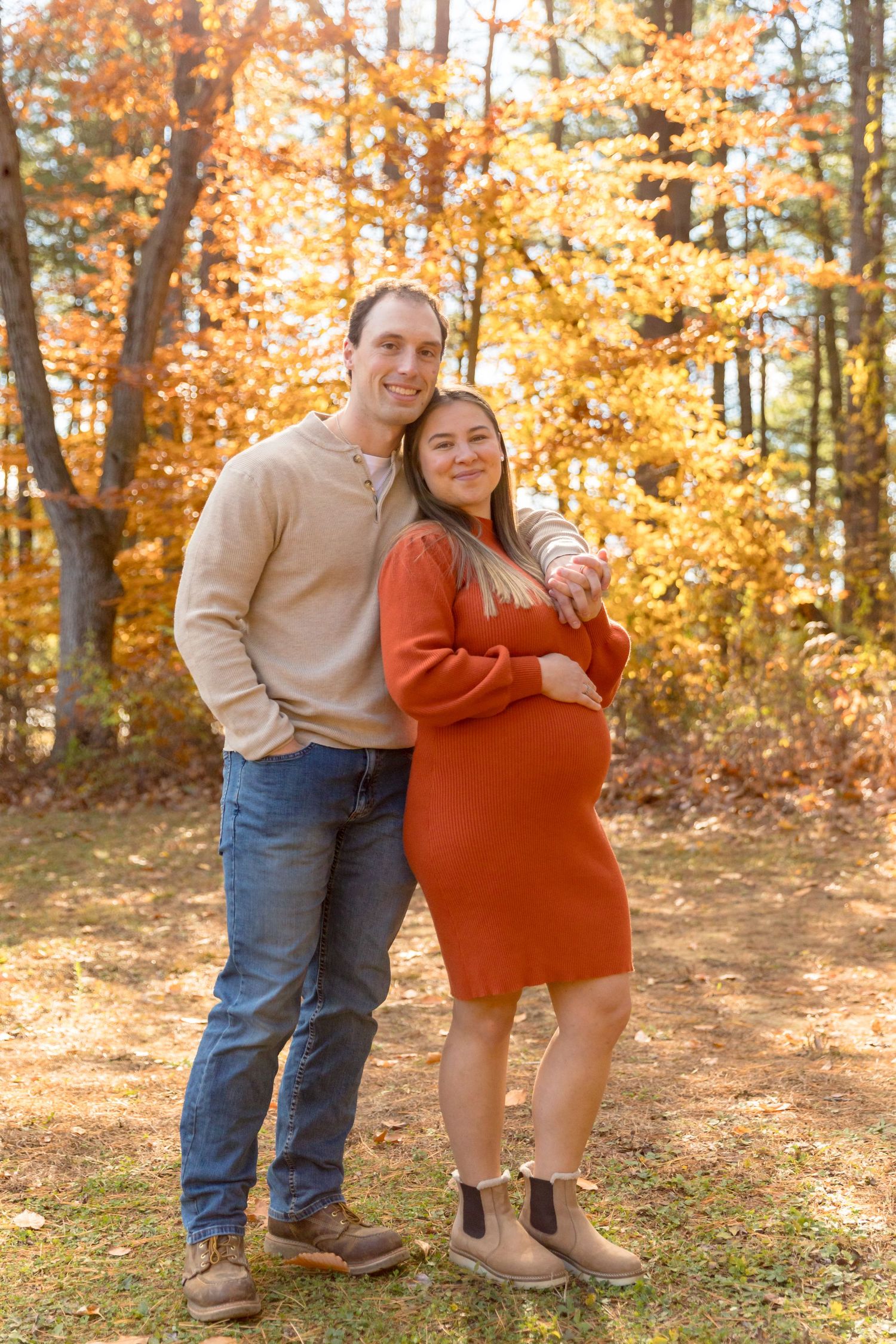A couple shares a tender moment in a sunlit autumn forest with golden leaves in the background.