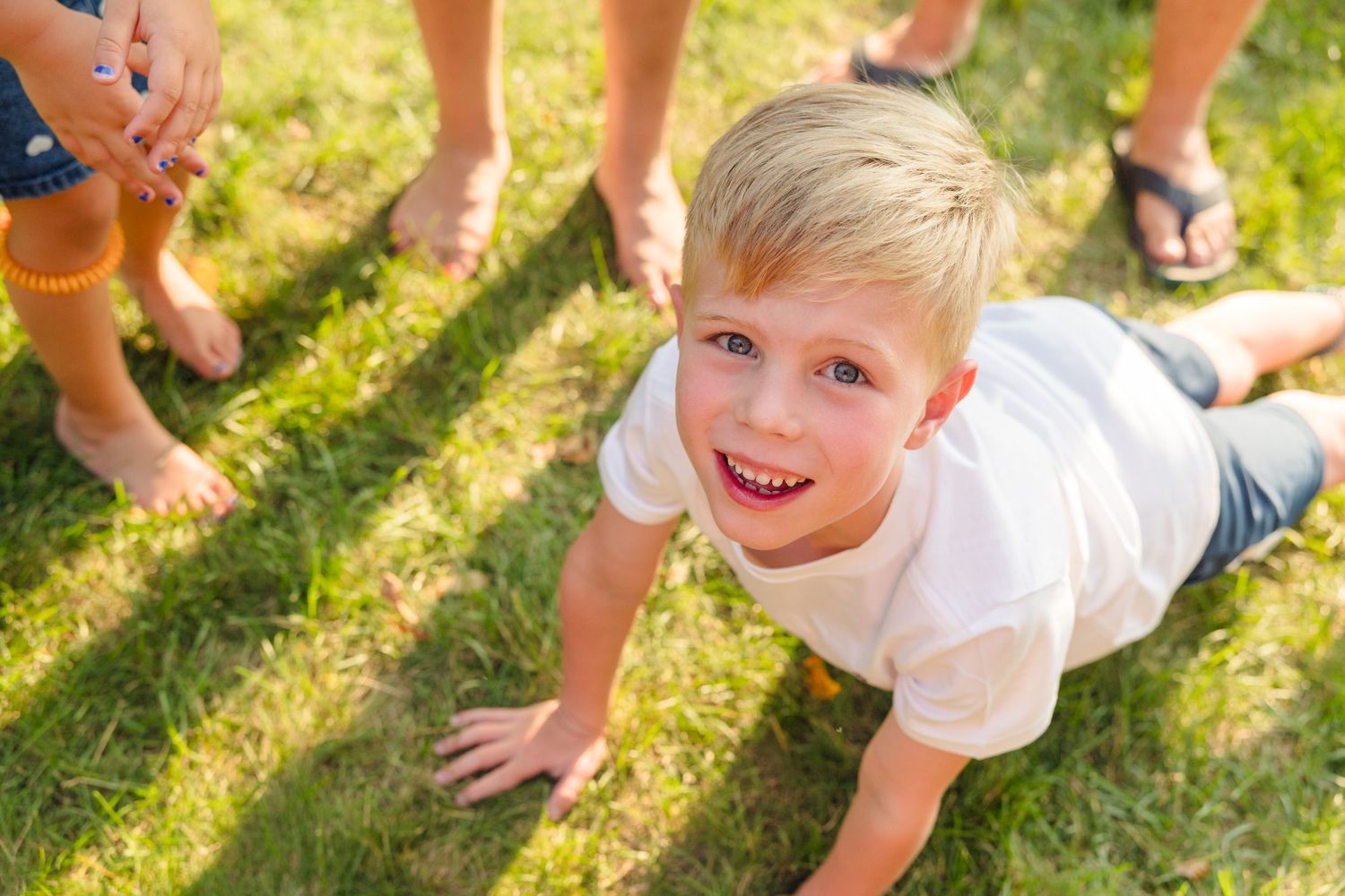 Children playing and laughing on grass during a sunny outdoor family photoshoot.