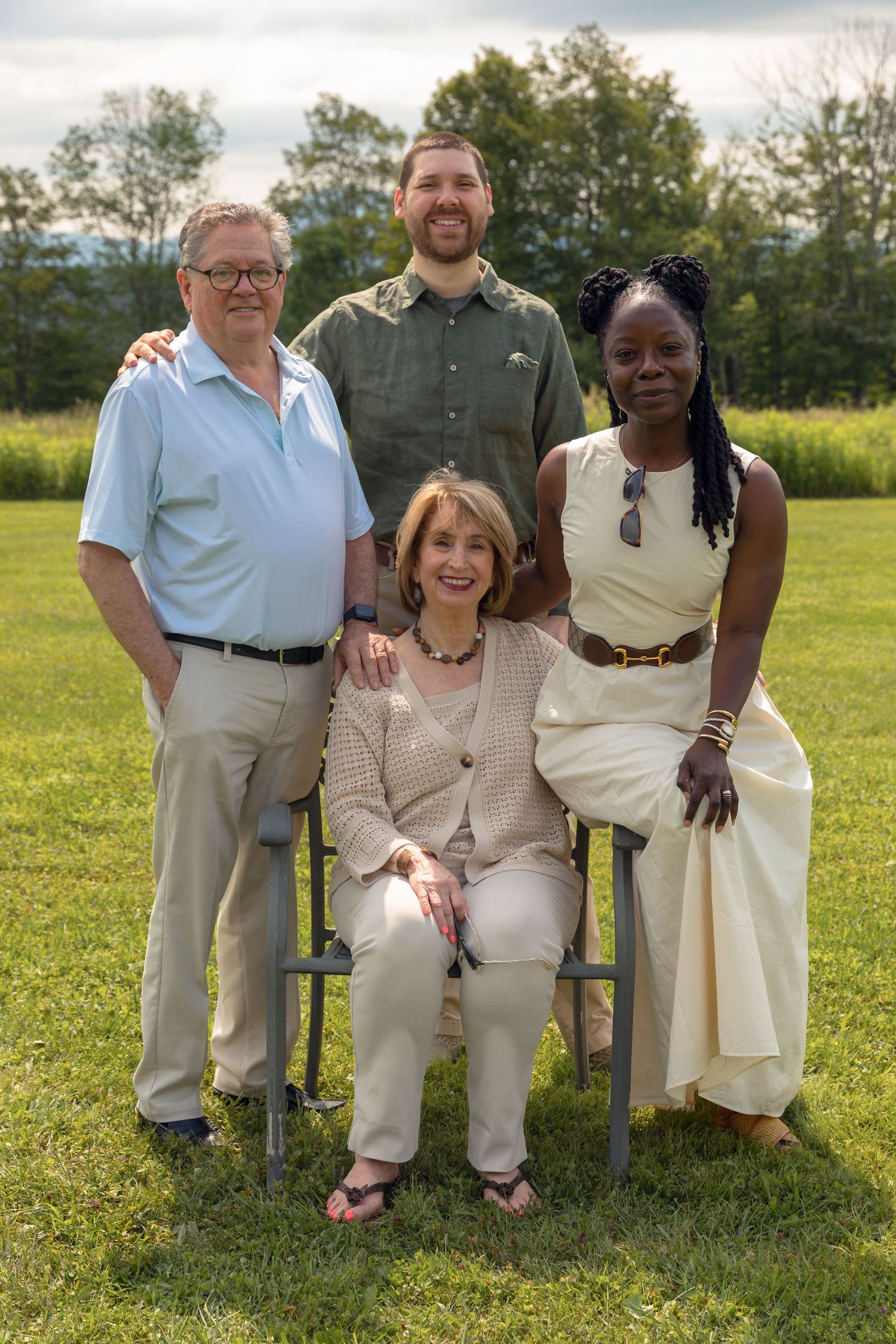 Multi-generational family group poses together on chairs outdoors in a sunny field.