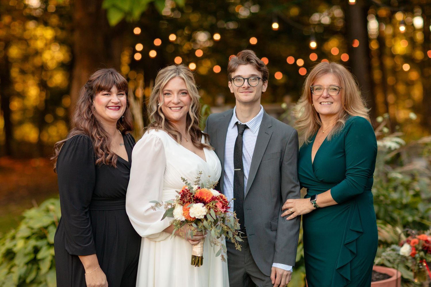Wedding party poses outdoors with autumn foliage and warm lighting in the background.