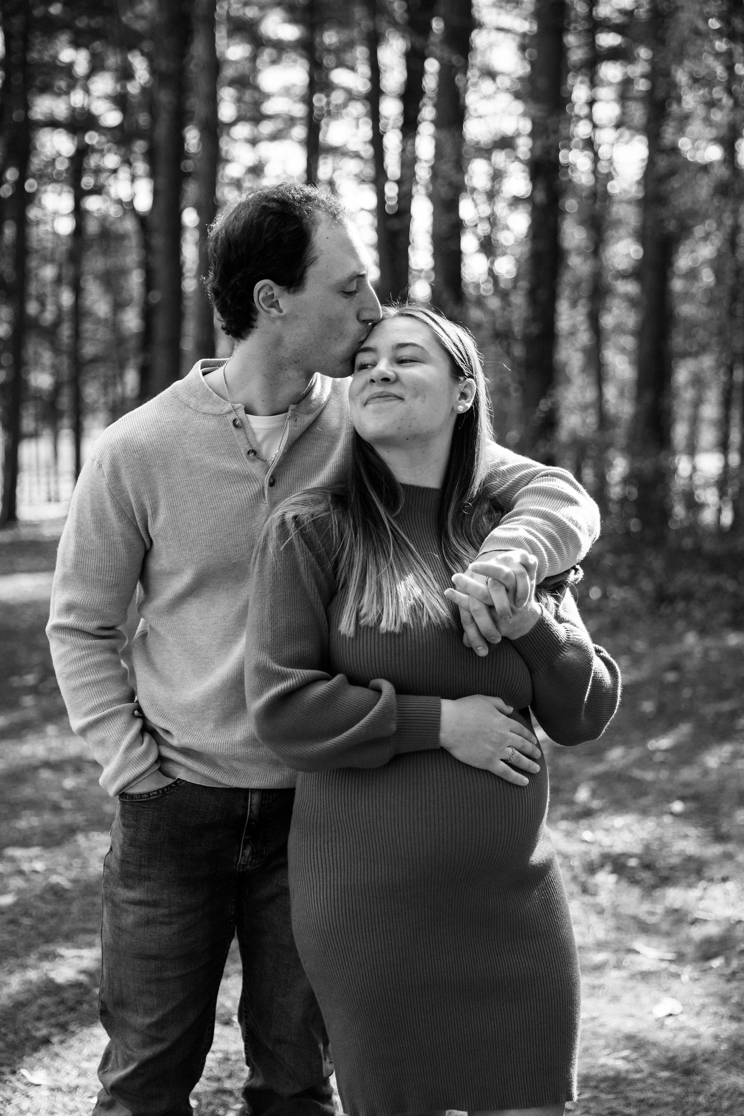 Black and white photo captures intimate moments between a couple in a forest setting.