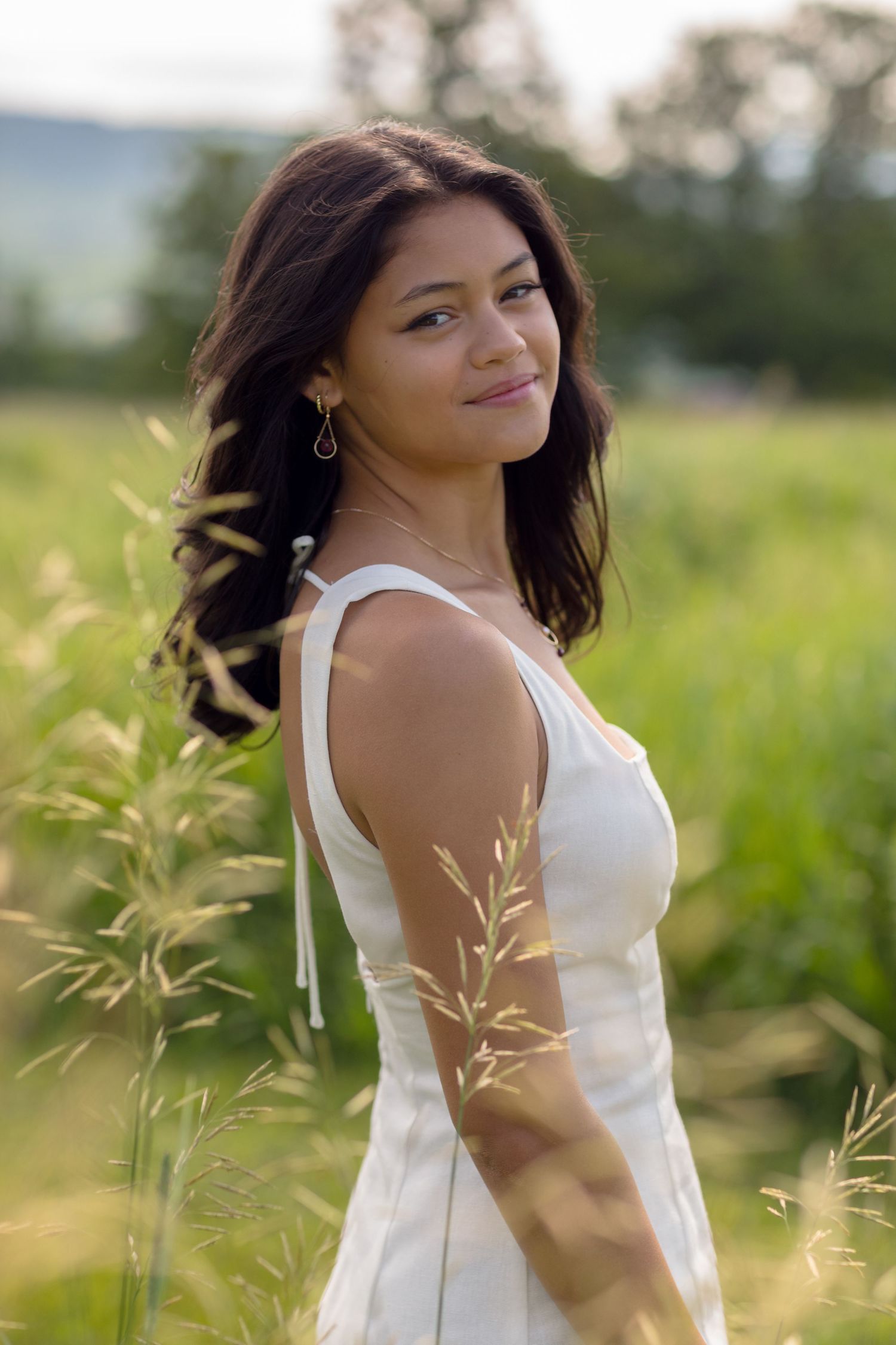 Graduate in white dress posing in field with tall grass during golden hour.