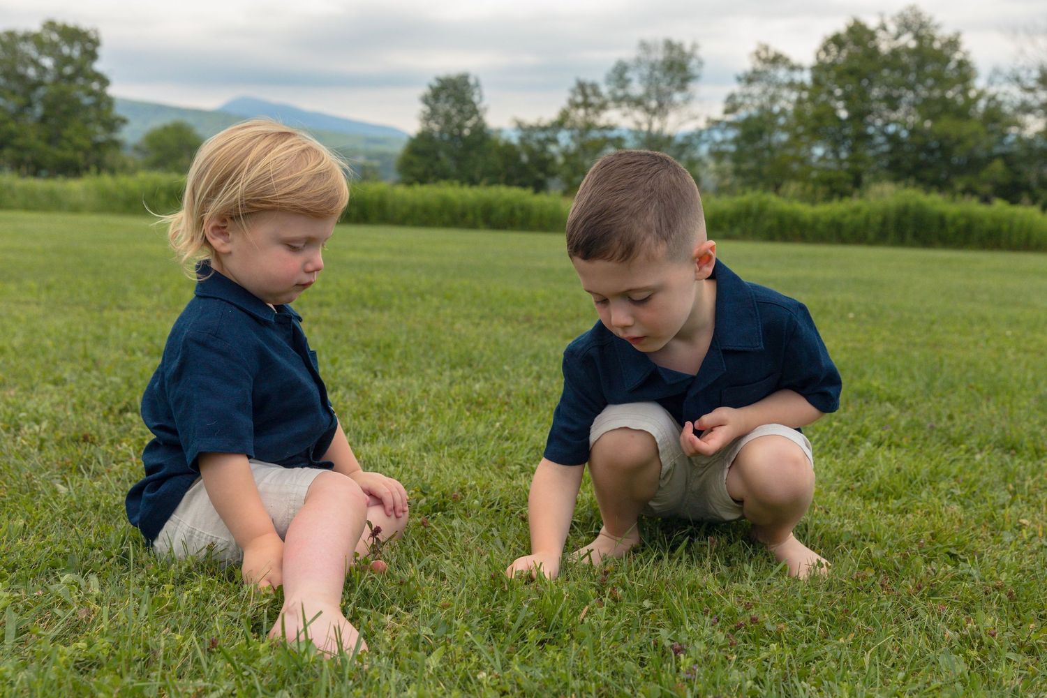 Children exploring and playing in the grass on a cloudy day.