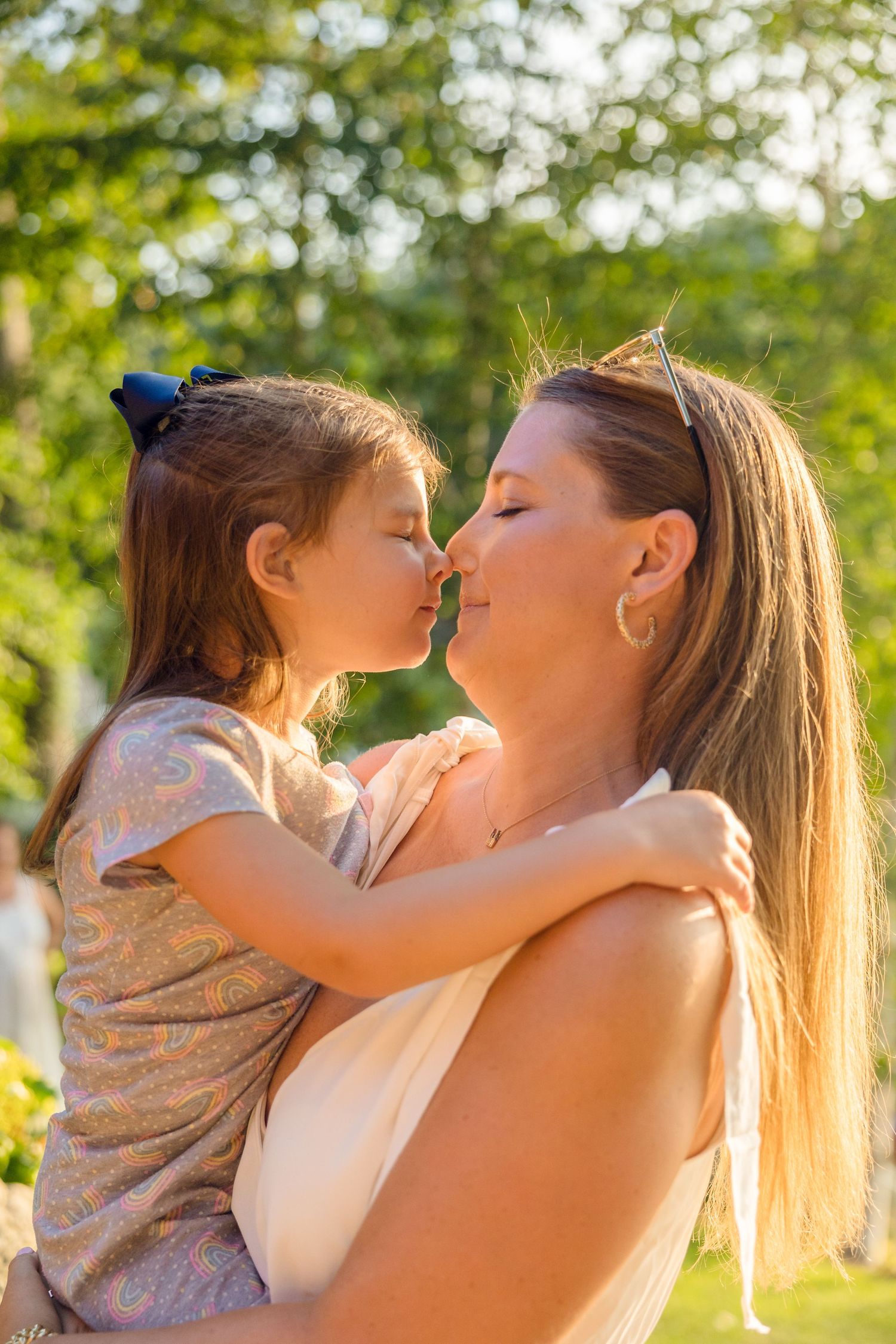 A tender moment between parent and child in golden sunlight with green foliage in the background.