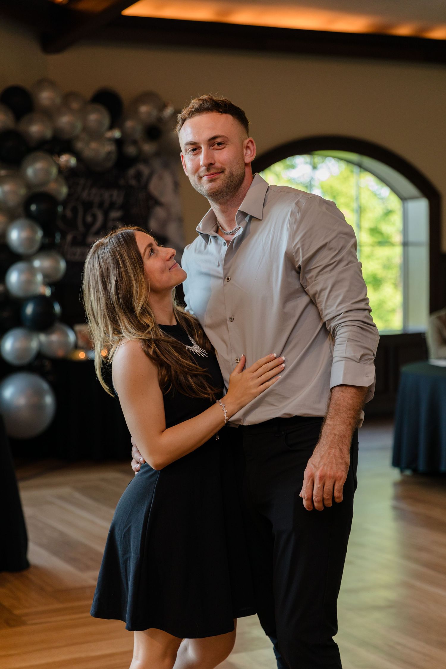 A couple sharing a romantic moment on a dance floor decorated with silver balloons.