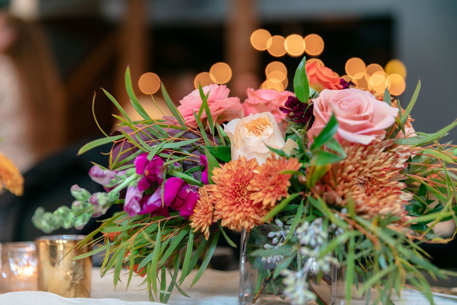 Elegant floral arrangement with pink roses and orange chrysanthemums on dark table.