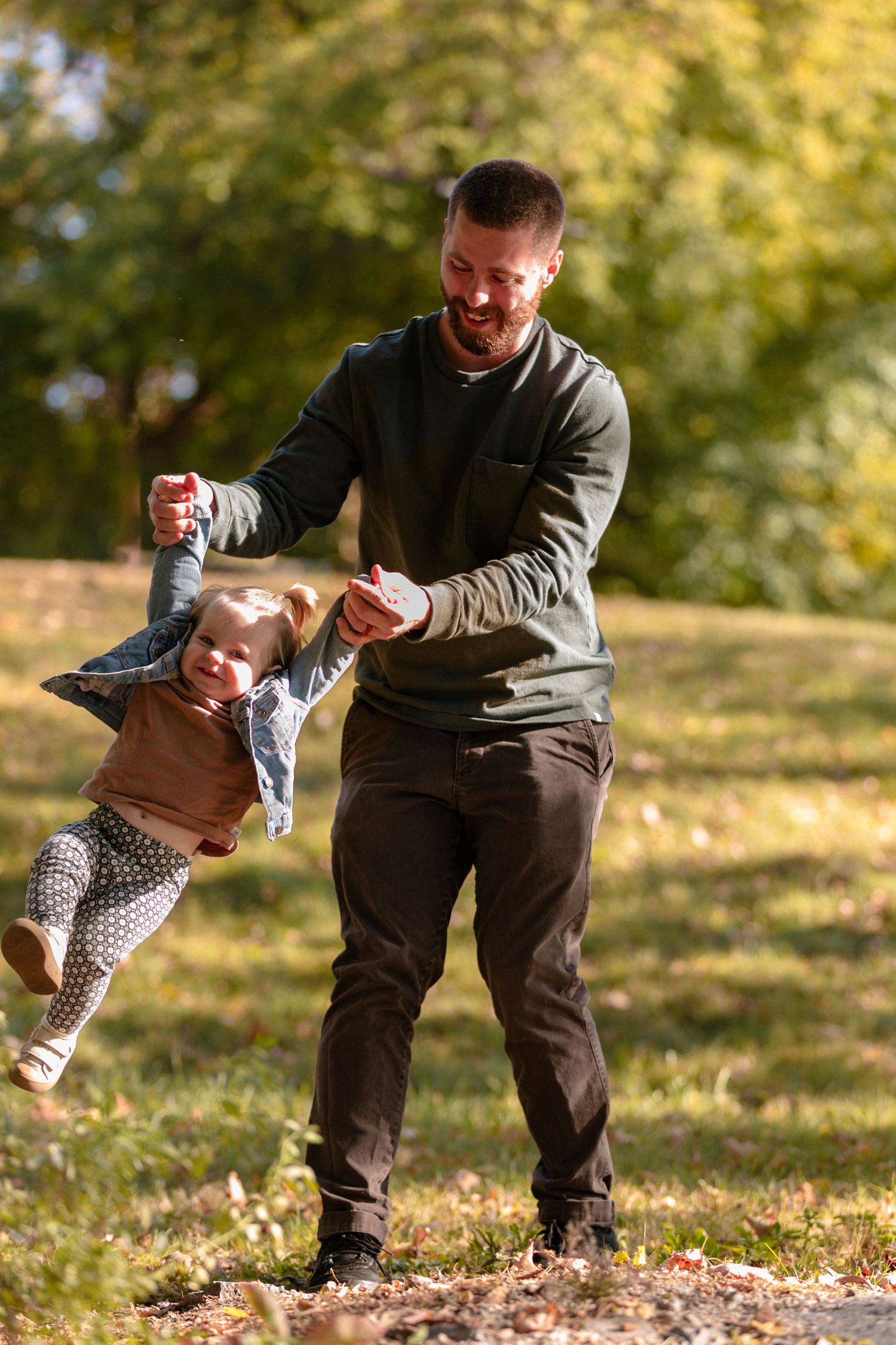 Parent swinging small child through air in playful autumn outdoor scene.