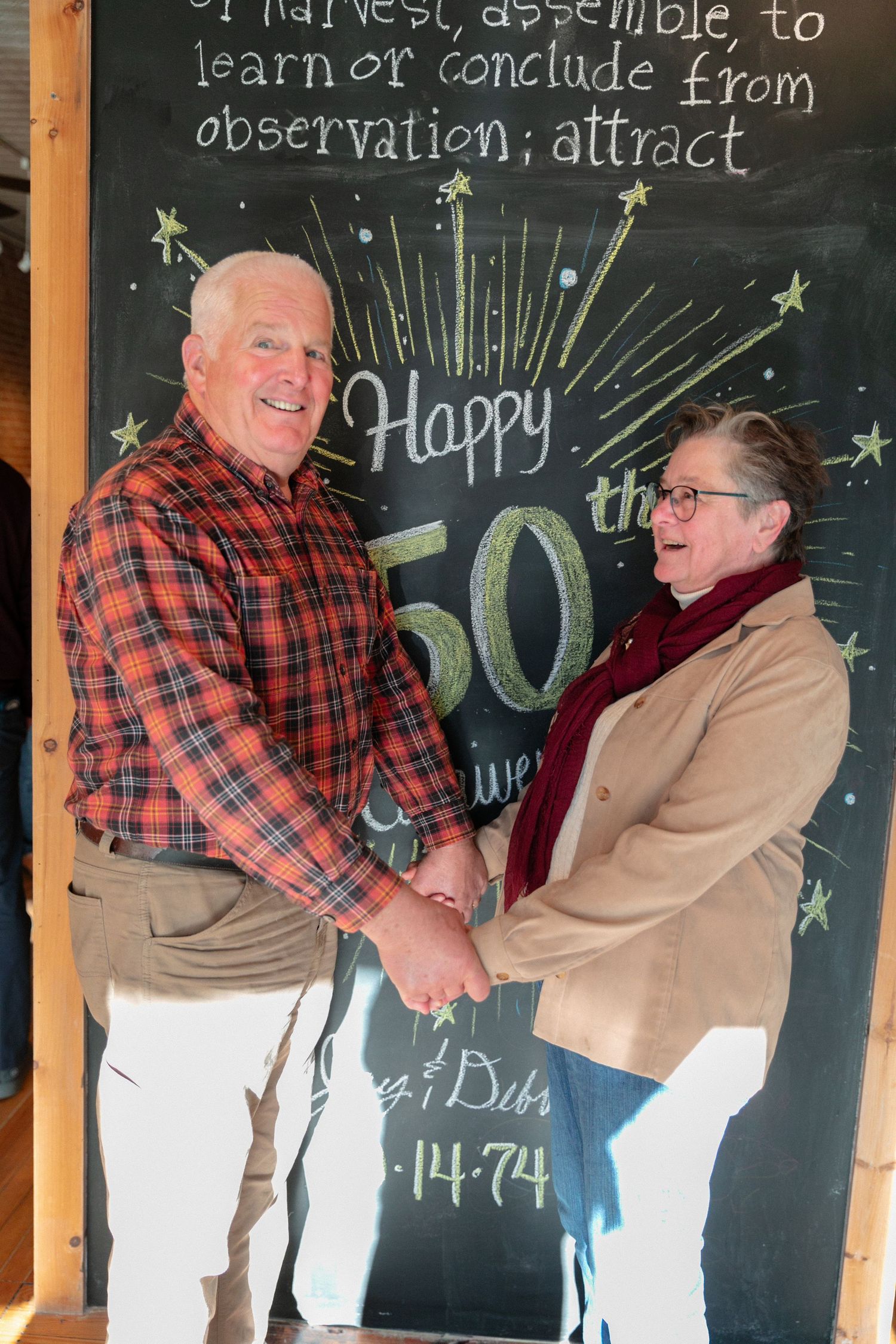 Couple posing playfully in front of a chalkboard sign at their anniversary celebration.