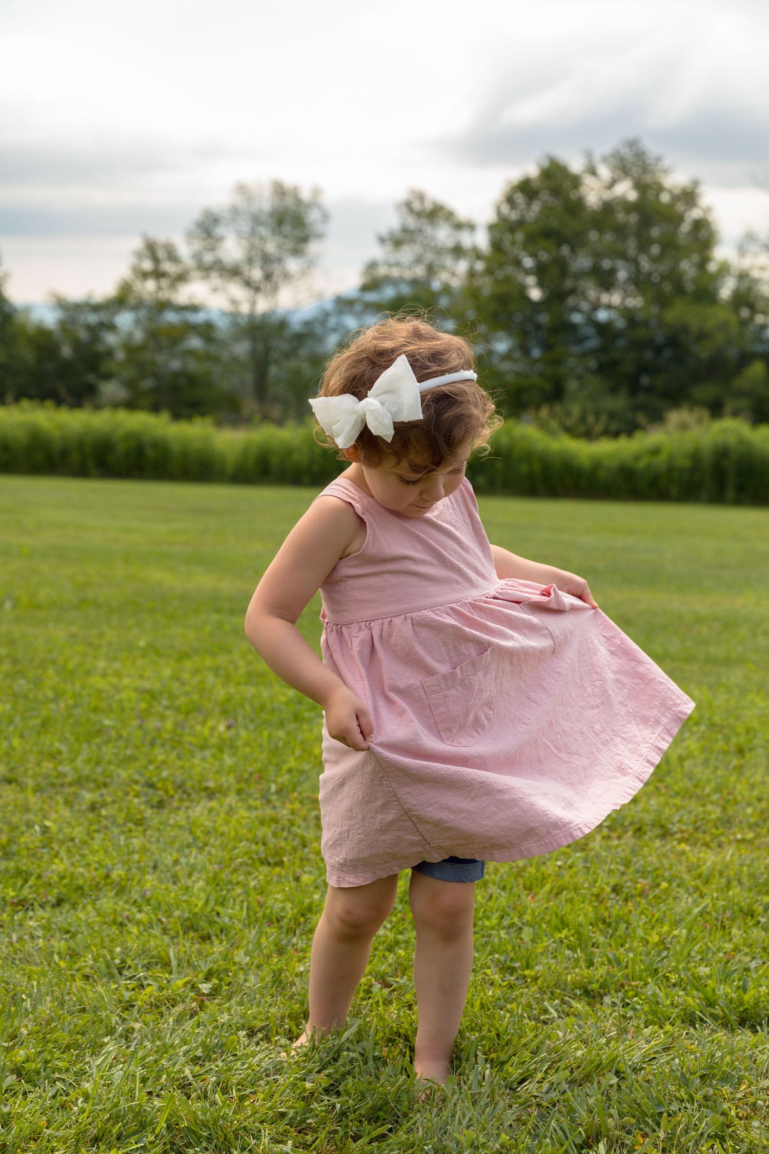 Young child in a pink dress twirling playfully in a grassy field on a summer day.