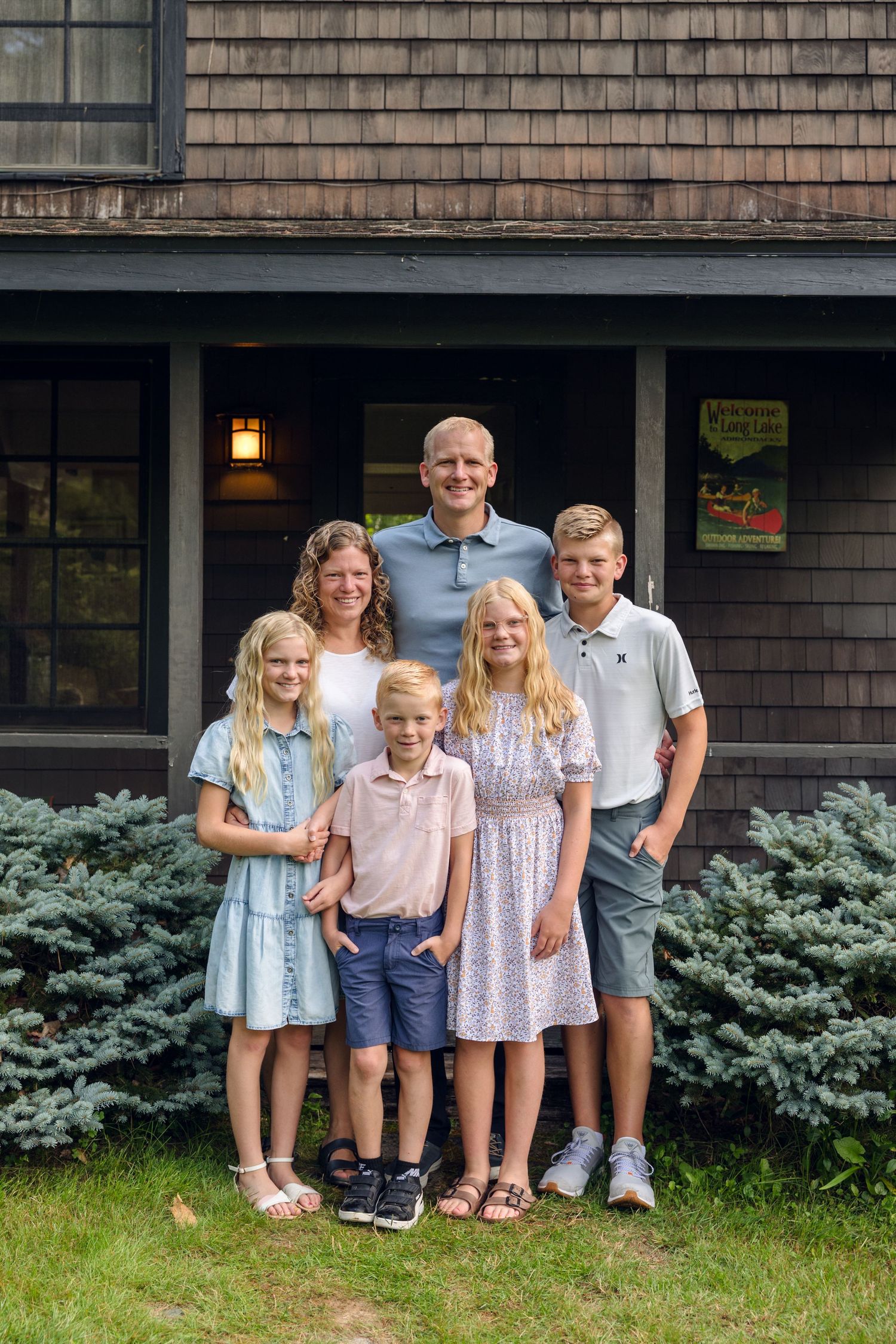 A group stands together for a portrait outside a cedar-shingled house with blue spruce bushes in the foreground.