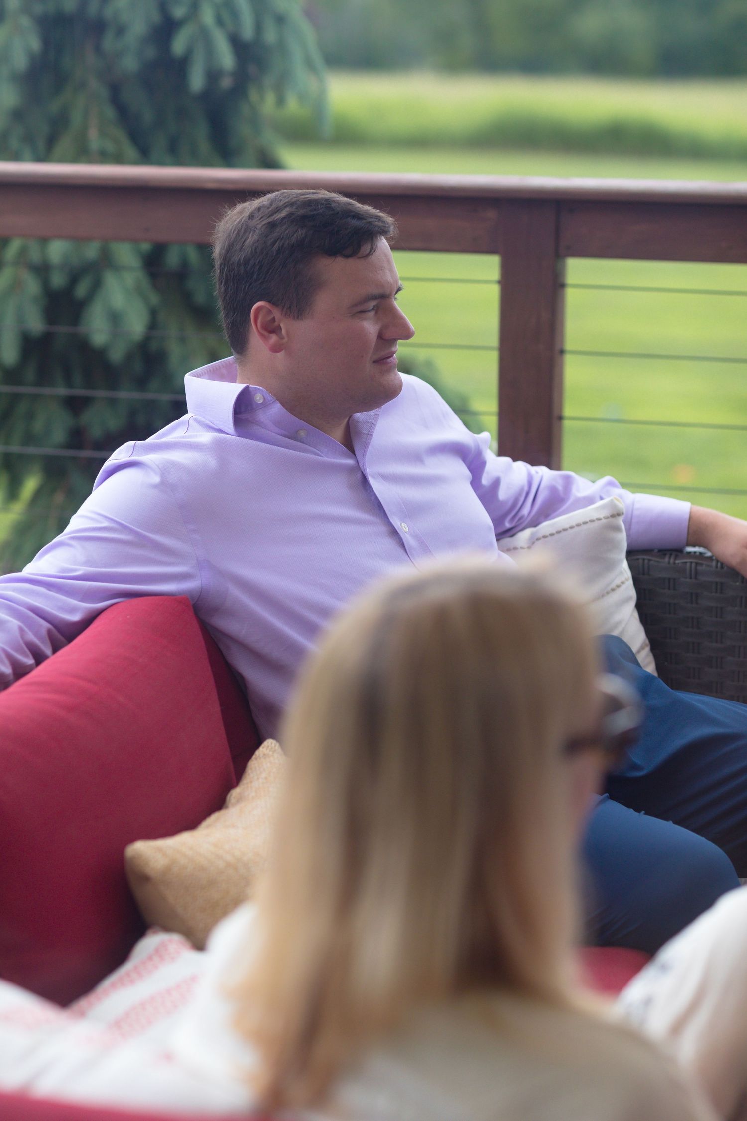 People relaxing on red cushions on an outdoor deck overlooking a green lawn.