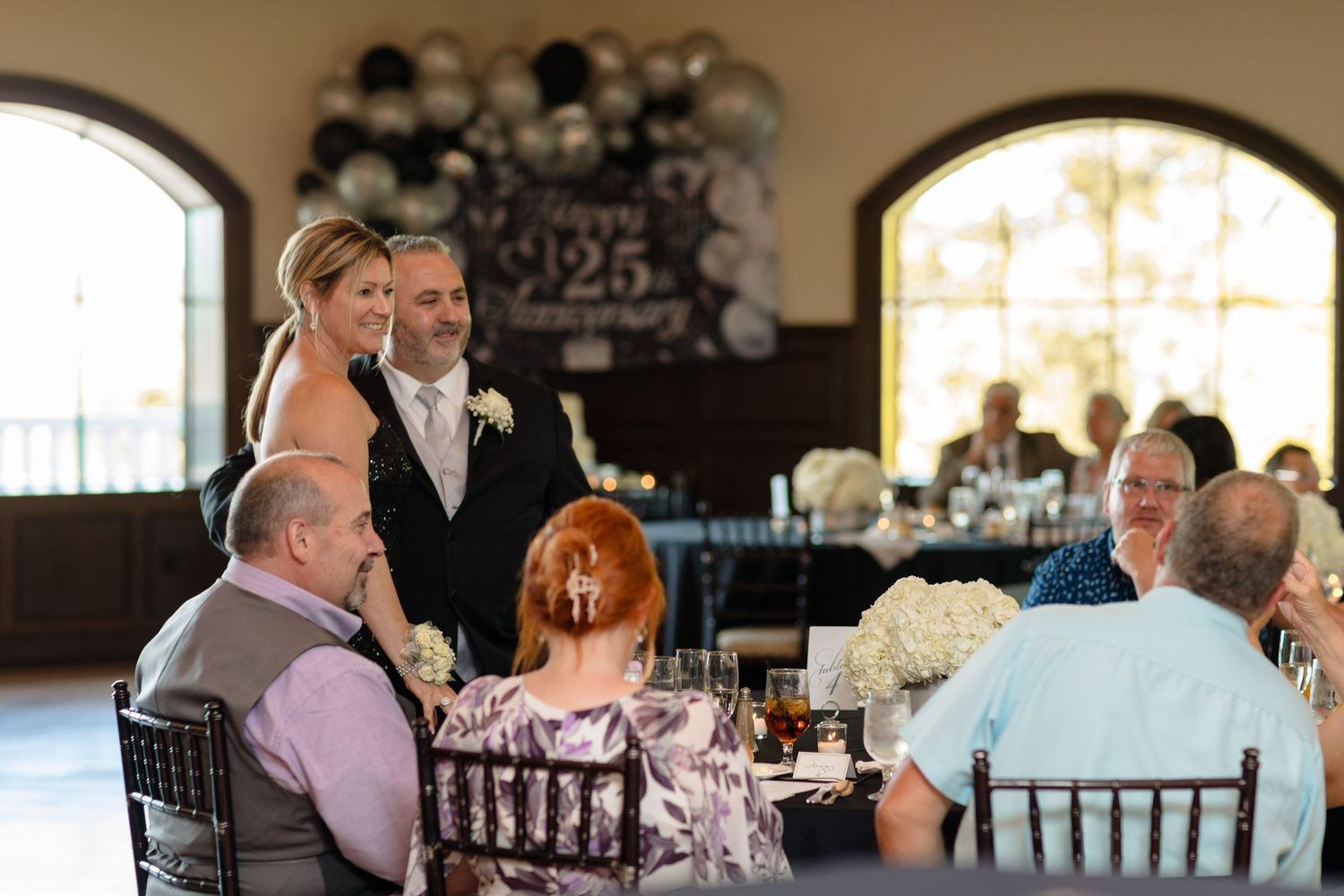 Guests seated at tables in a banquet hall with arched windows and elegant decor.