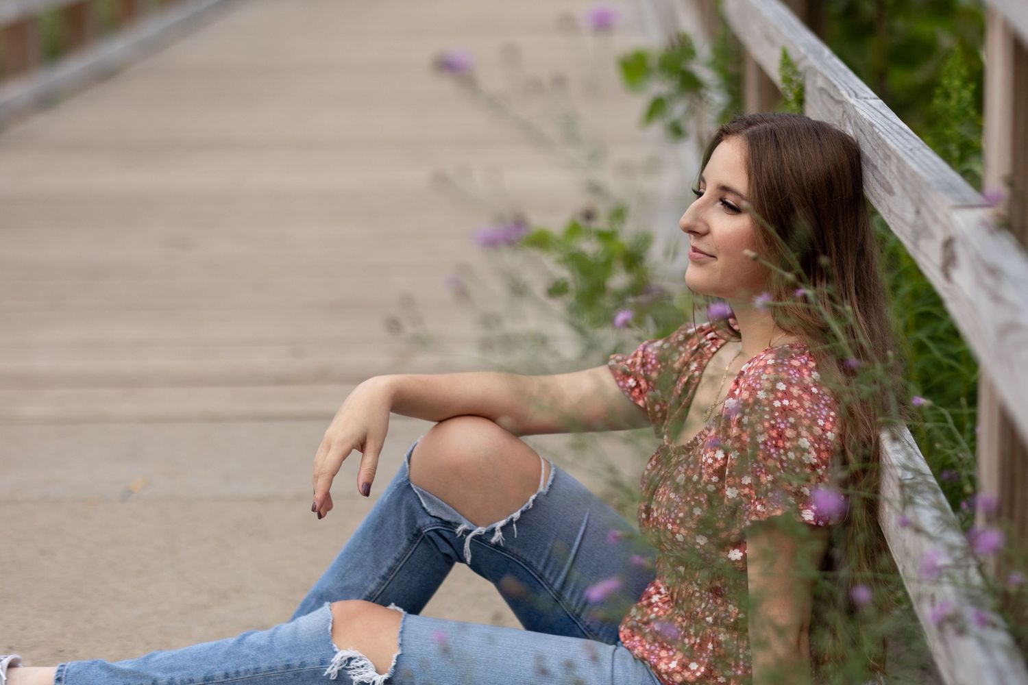 Portrait session in casual attire sitting on concrete path with greenery in background.