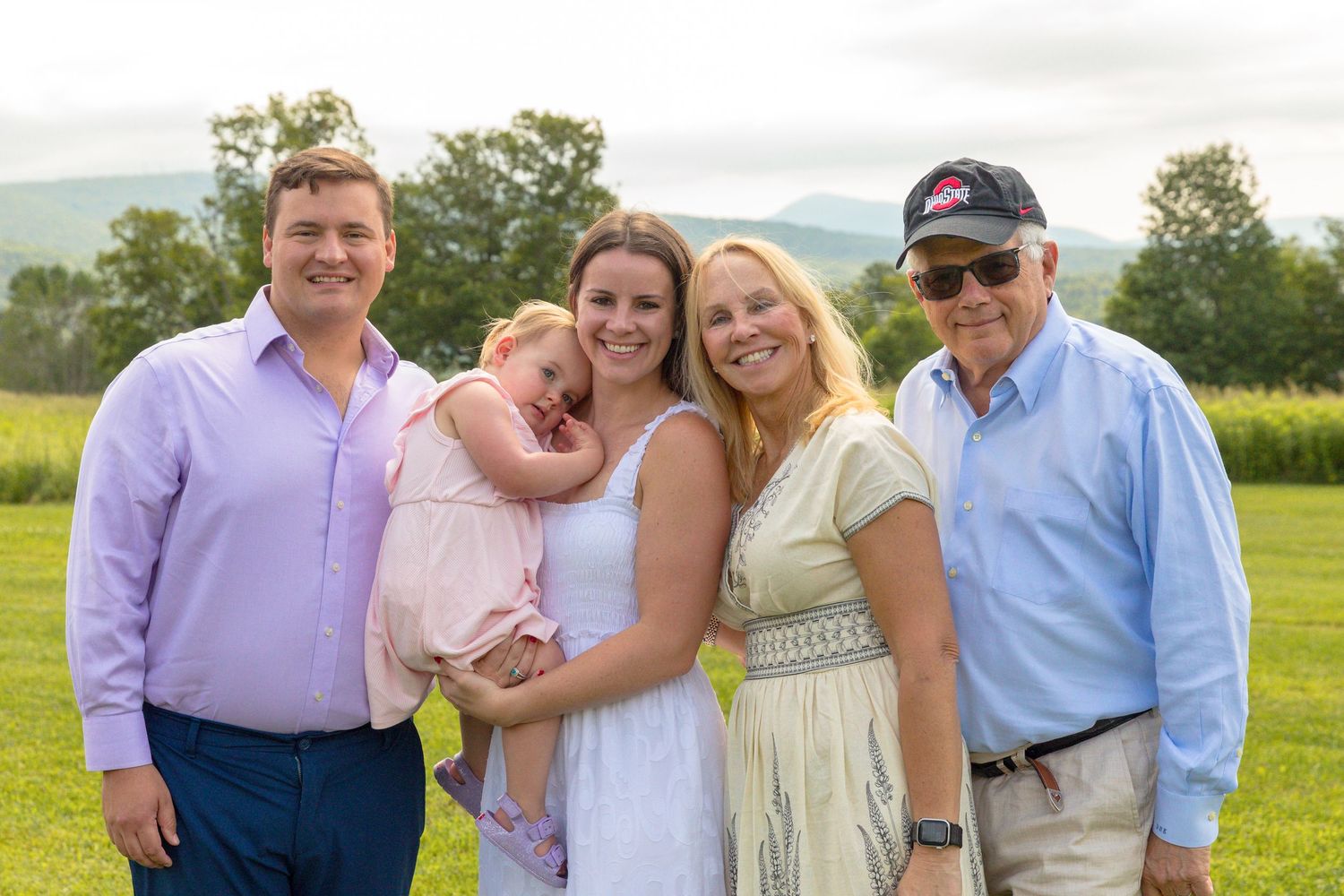 Wedding party and family members posed together in pastel colors on a sunny hillside.