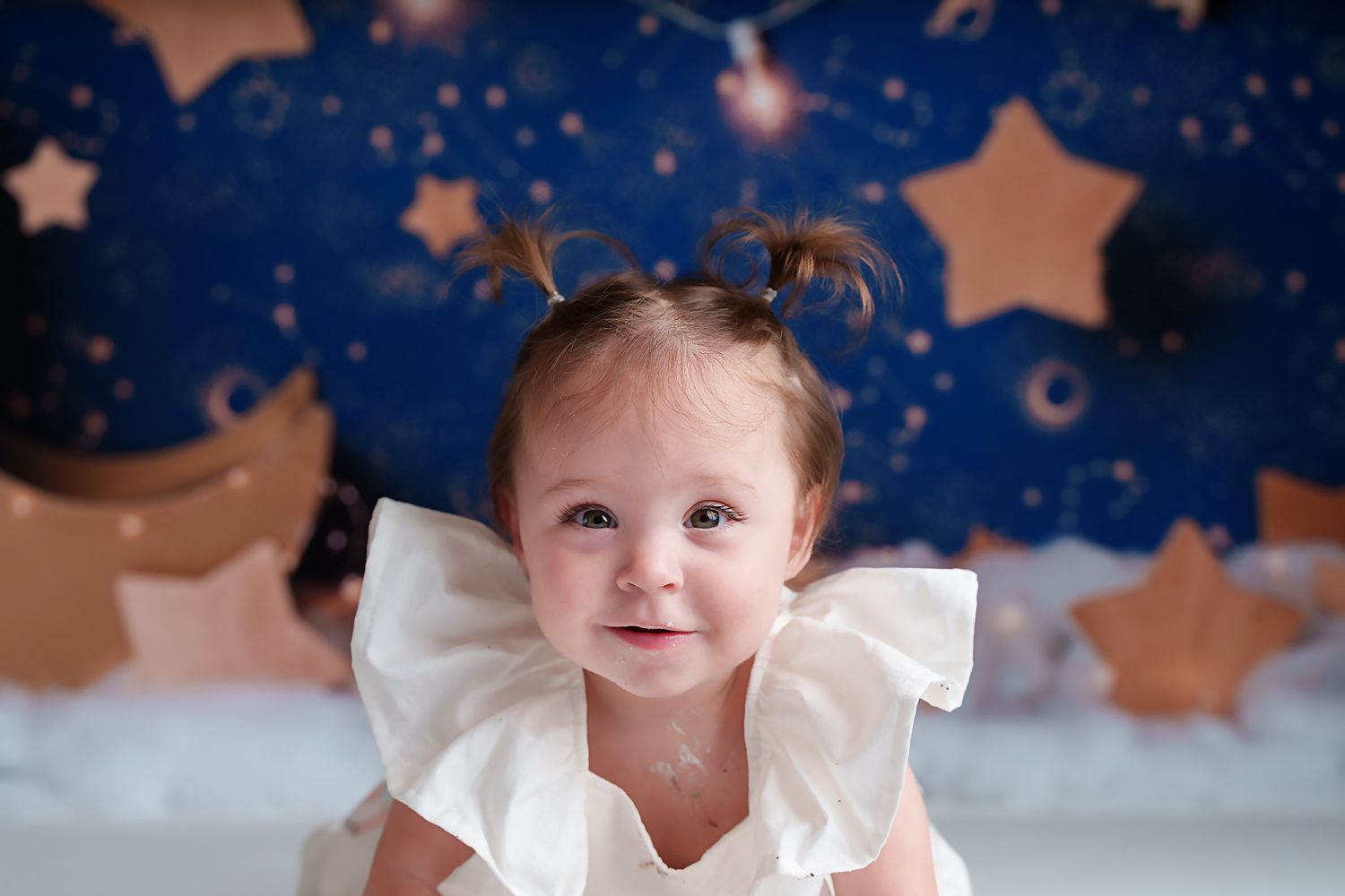 Close-up image of a 1 yr old girl smiling with a dark blue and gold celestial backdrop behind her during a Lexington SC Cake Smash Session.