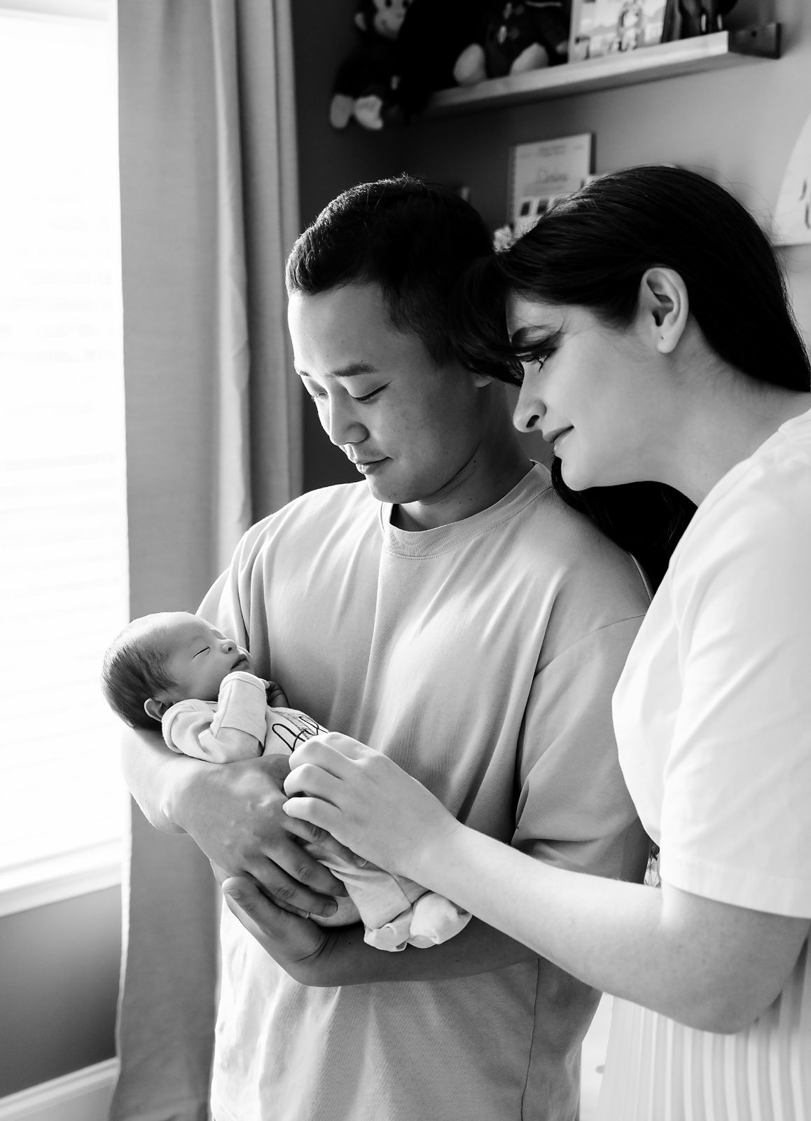 Sweet and cozy image of parents holding their newborn baby boy as window light embraces them during a Lexington SC in-home newborn session.