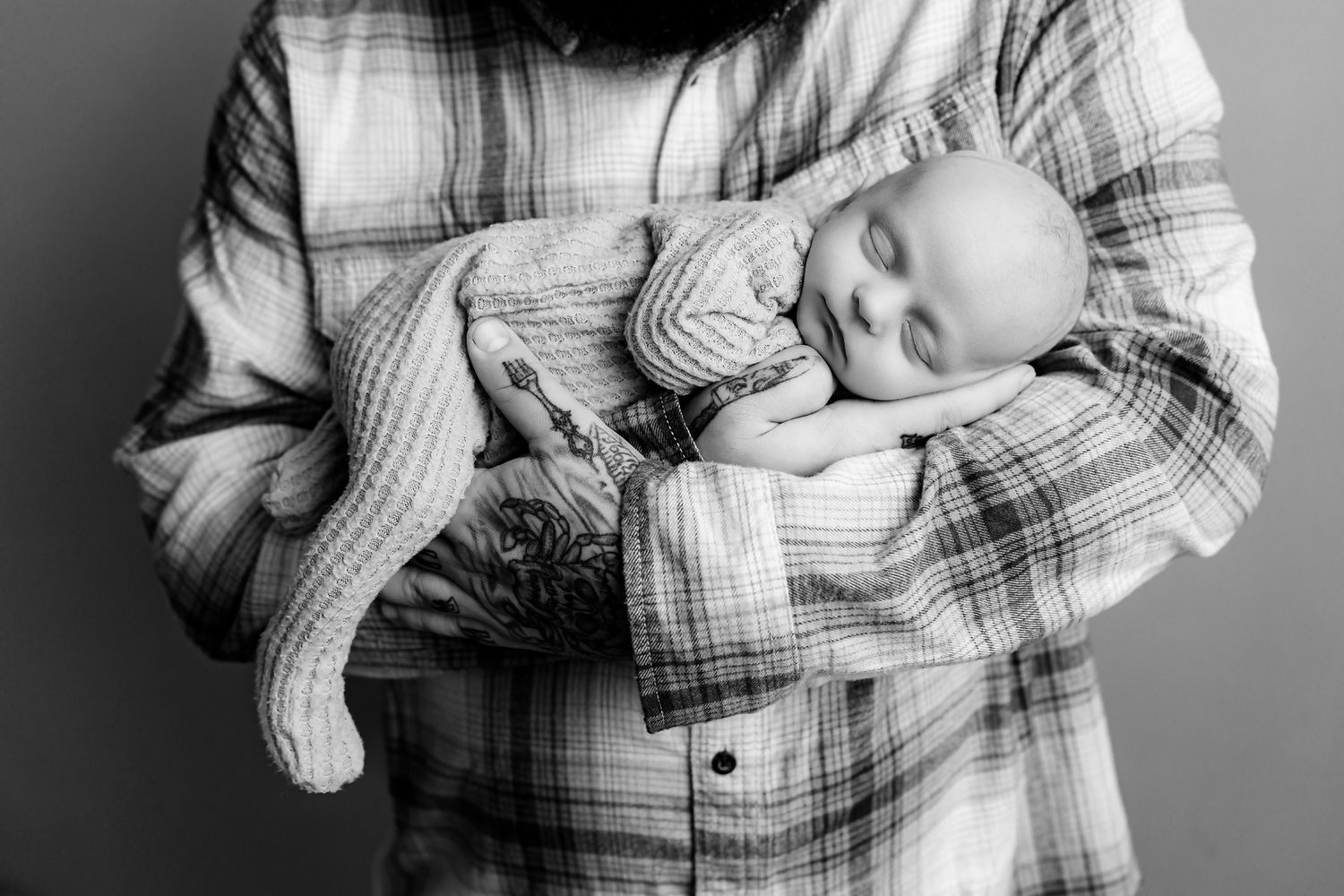 Dad in a plaid shirt cradling his newborn son in his arms during a Studio Newborn Session for clients from Newberry SC.