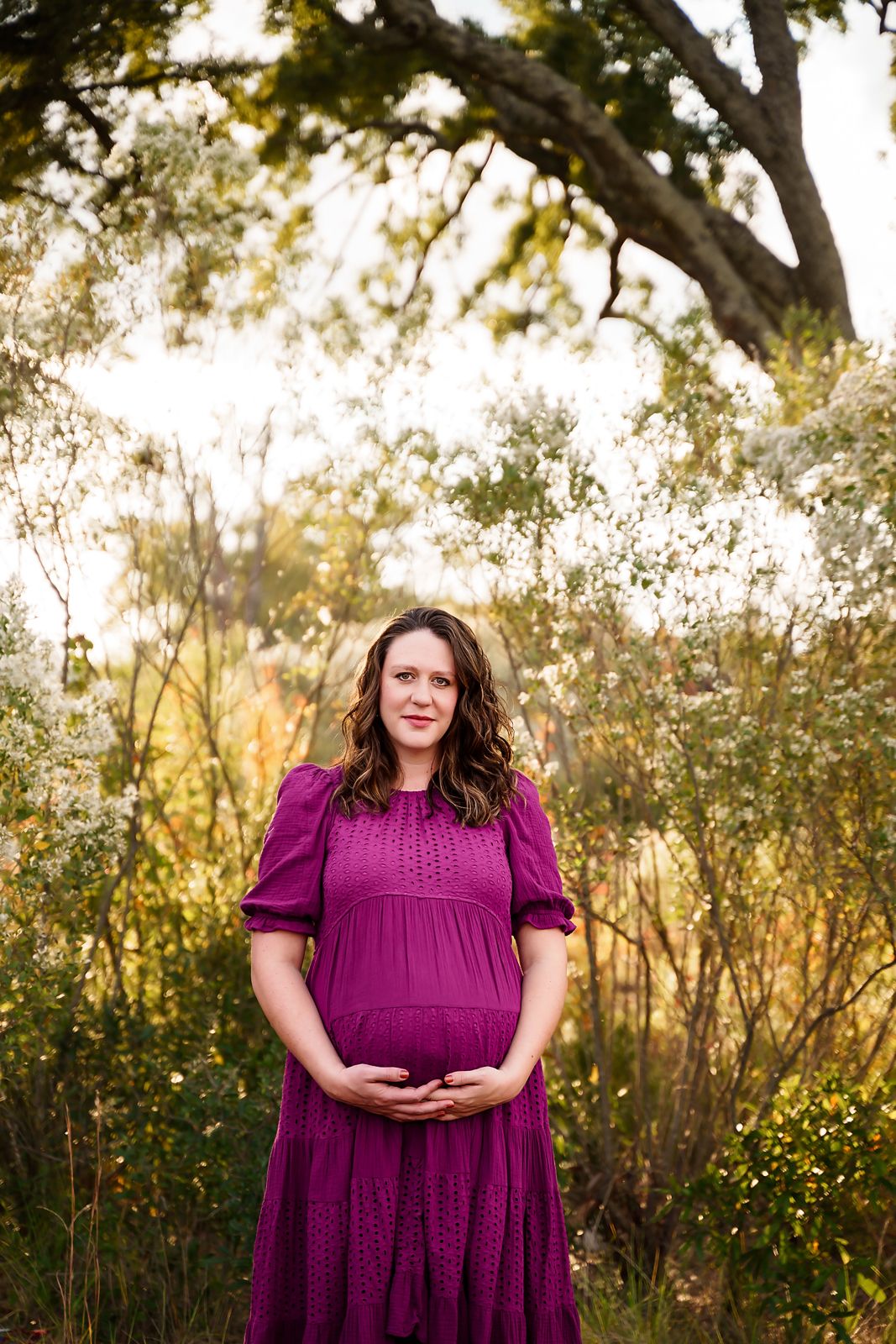 Stunning outdoor maternity portrait of Mom in front of a gorgeous tall tree with light glowing behind her during a Lexington SC Session.