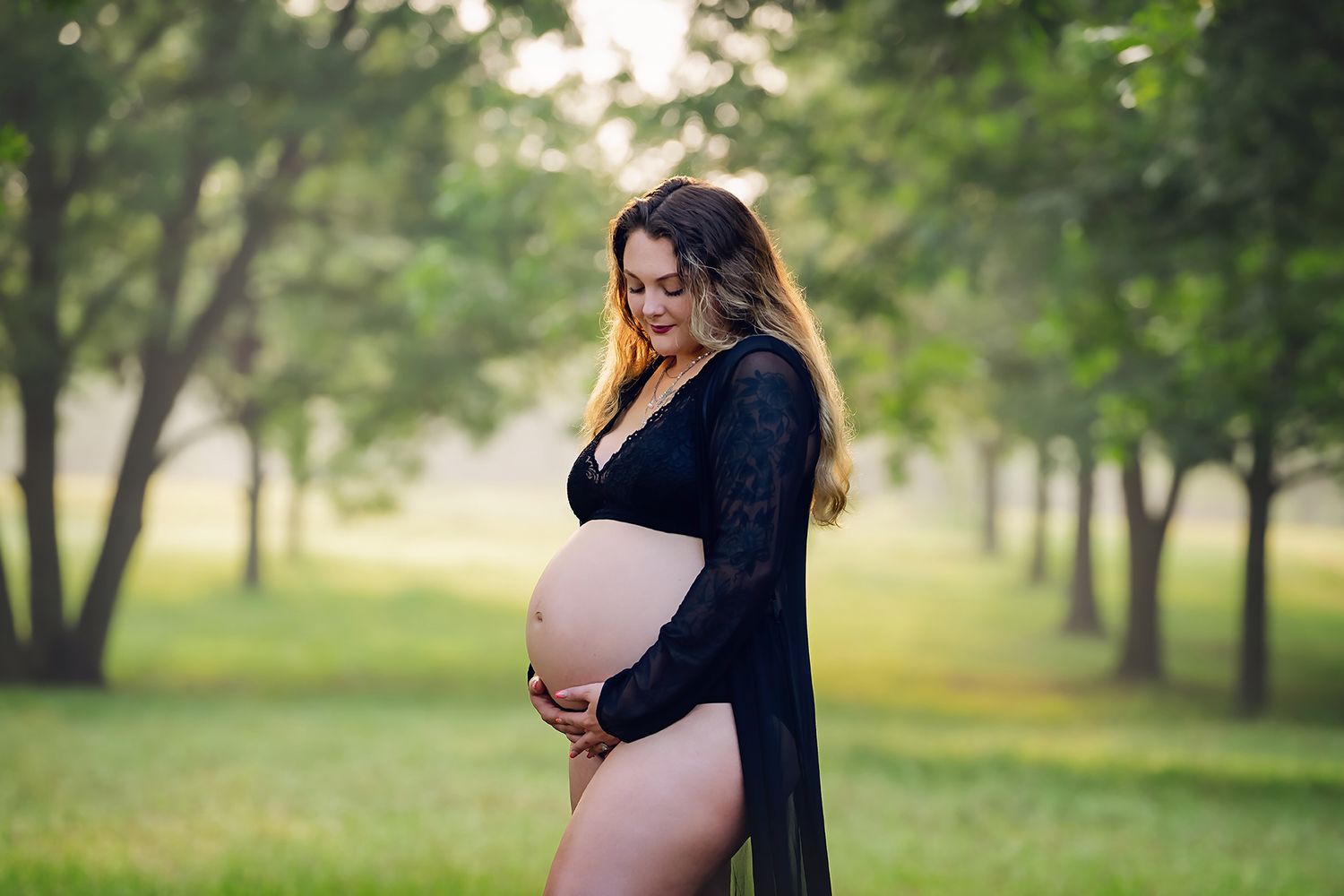 Stunning Mom to Be looking down at her baby bump while standing in between a row of pecan trees during a Lexington SC Maternity Session.
