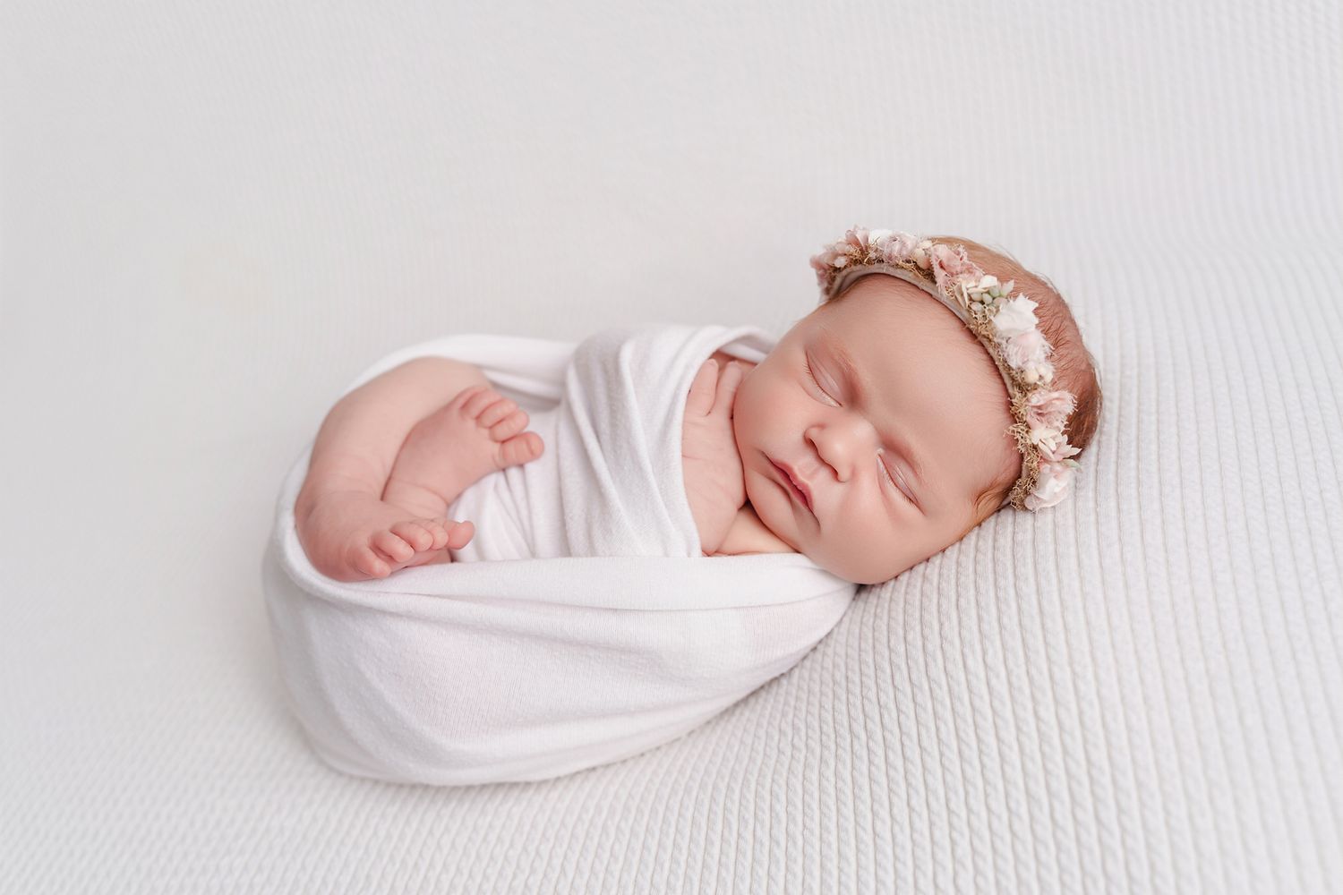 Baby girl in a white swaddle with her feet visible and posed simply on a white background during a studio newborn session in Chapin SC.