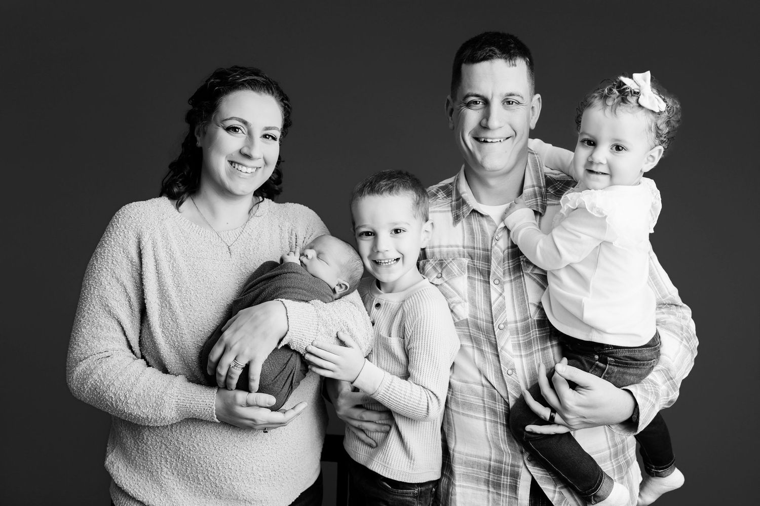 Black and White family image with Mom holding a newborn while Dad holds their other two older children during a Studio Newborn Session in SC