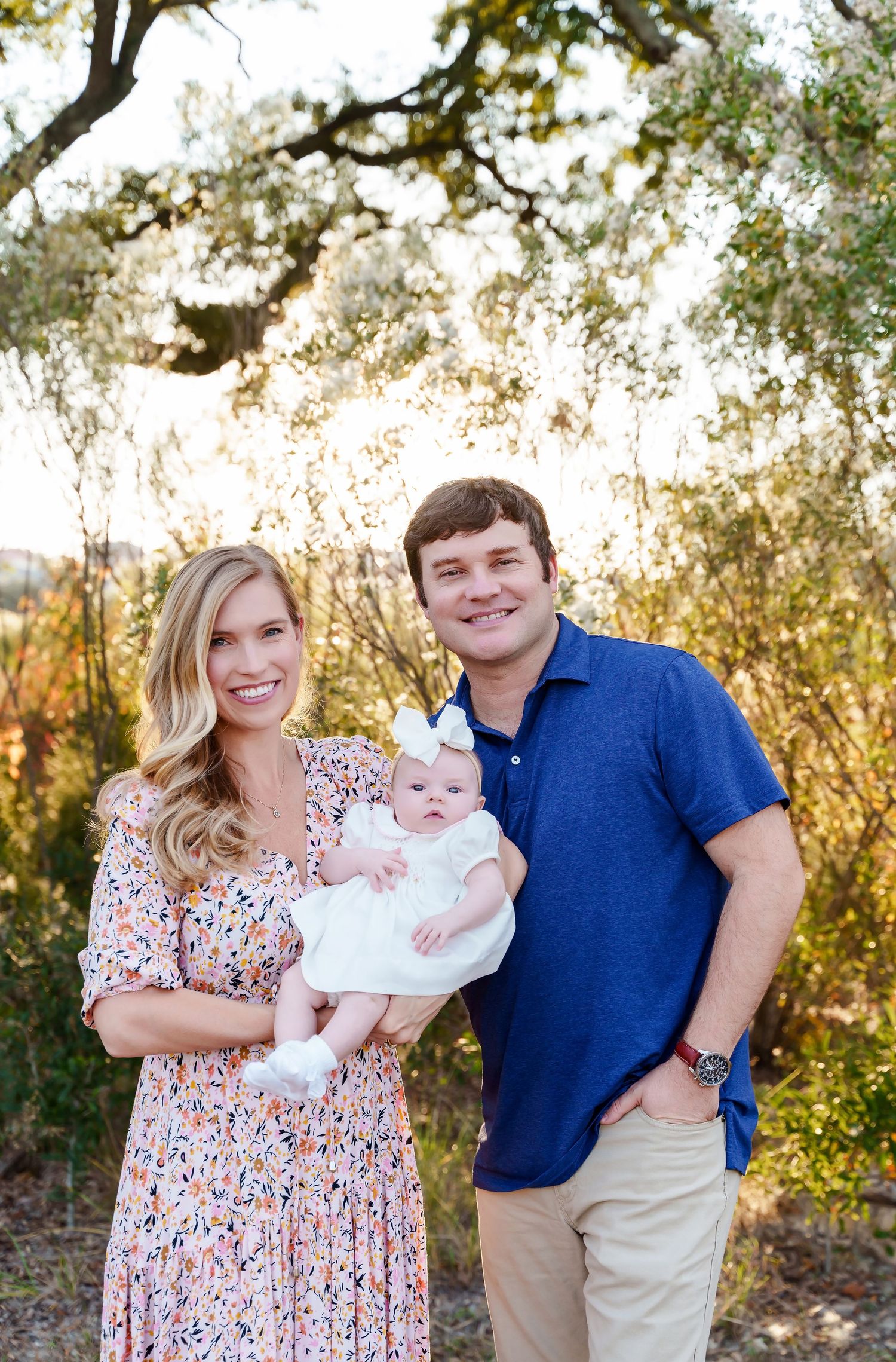 Mom and Dad cradling their young baby in front of a gorgeous sunset lit greenery backdrop during a Family Portrait Session in Columbia SC.