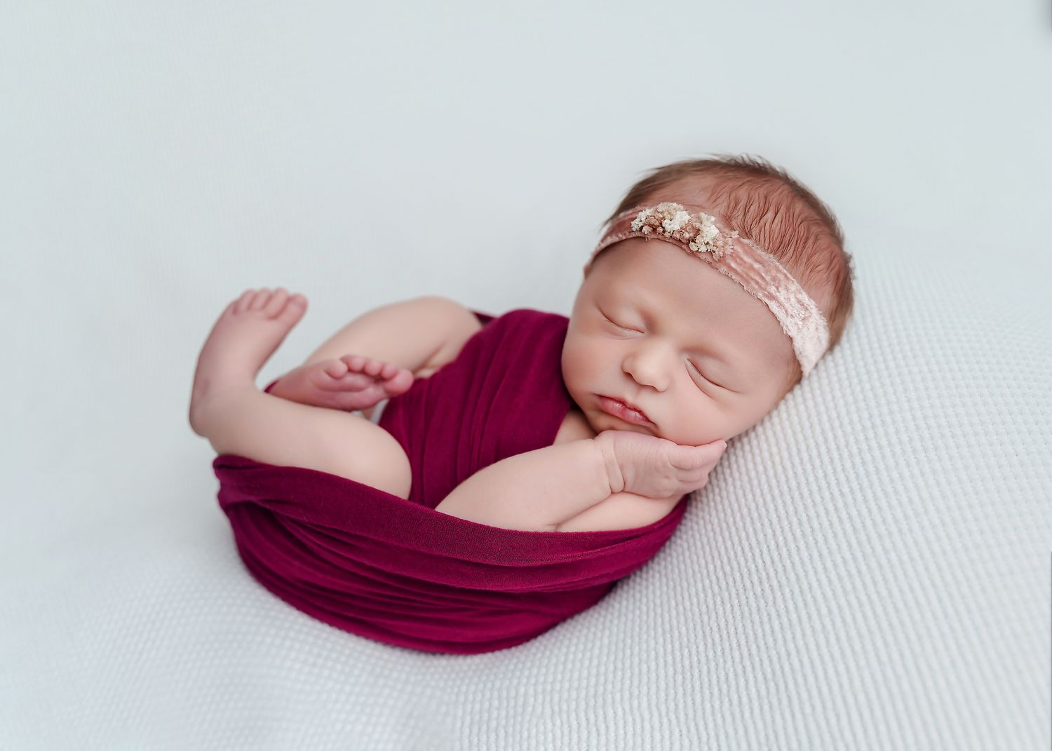 Baby girl swaddled in red wrap so that her feet and hands show while posed on a white backdrop during a Lexington SC Studio Newborn Session.