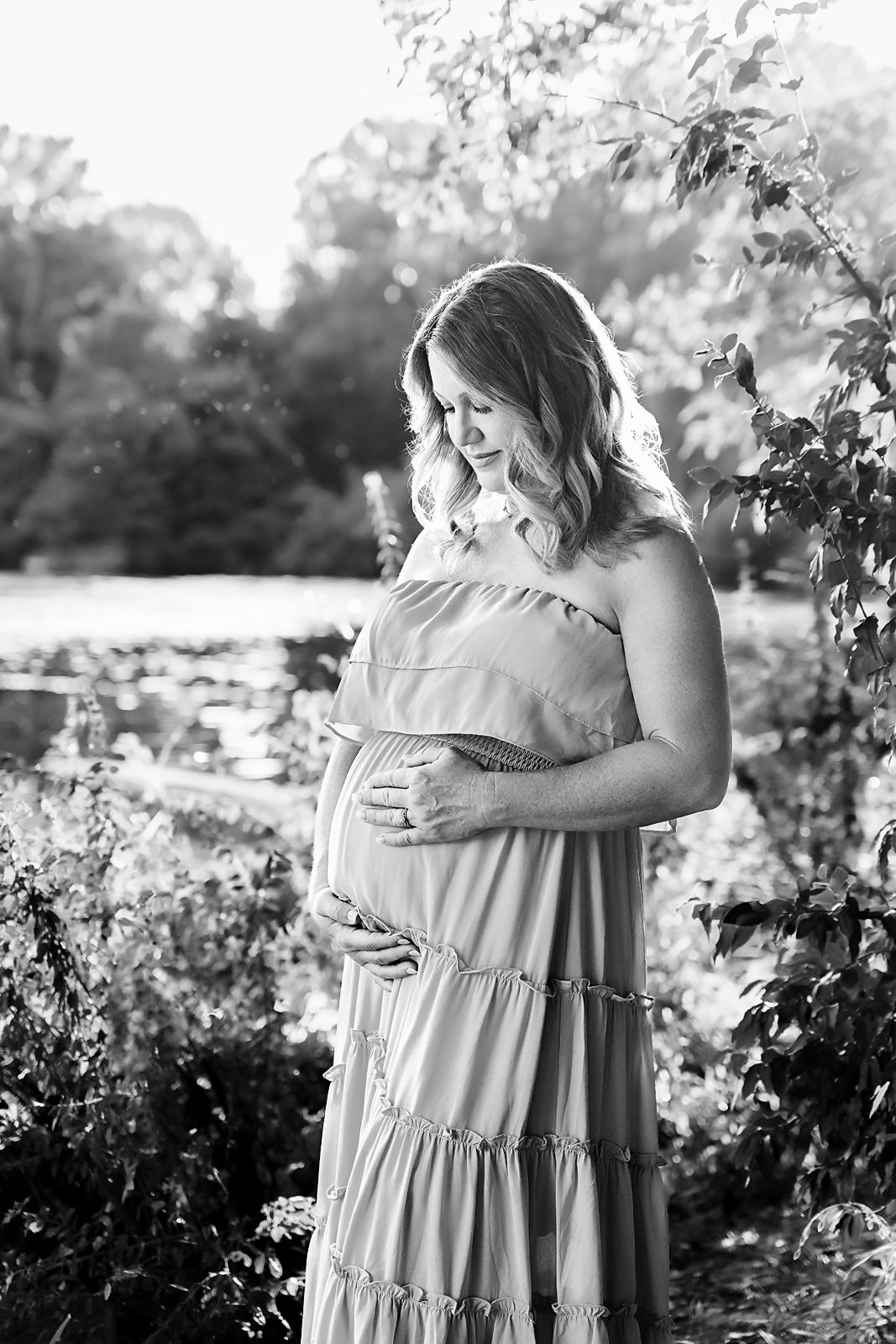 Black and White image of mom to be by the river with branches embracing the edges of the image during a Columbia SC Maternity Session.