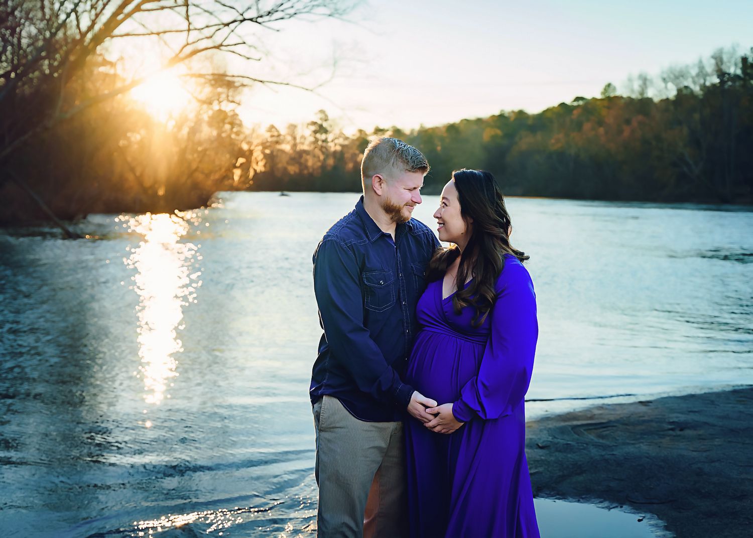 Stunning riverwalk winter Maternity Portrait Session in Columbia SC featuring the couple posing with water and sunrise in the background.