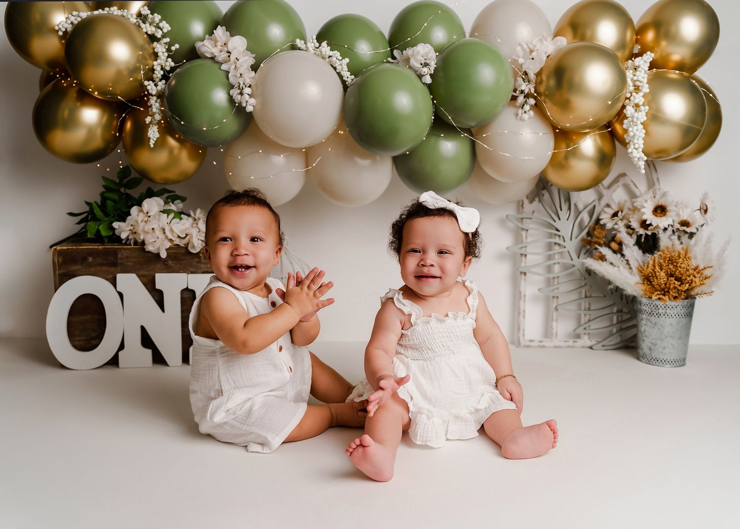 Columbia SC 1st Birthday Studio Portrait Session for twins featuring sage green, cream and gold colors with a balloon garland behind them.