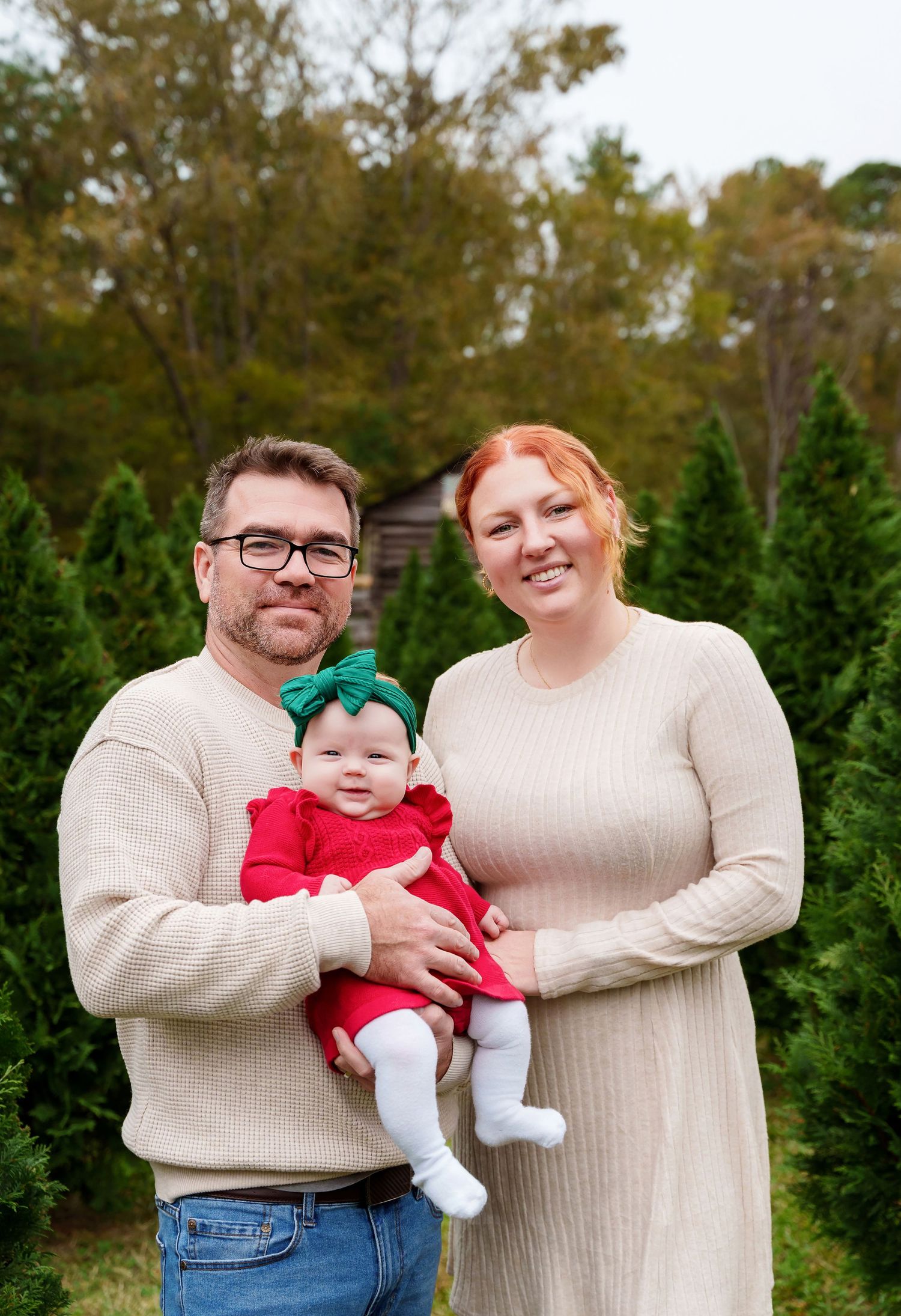 Mom and Dad holding their smiling young baby during a Christmas Tree Farm Mini-Session in Chapin SC.