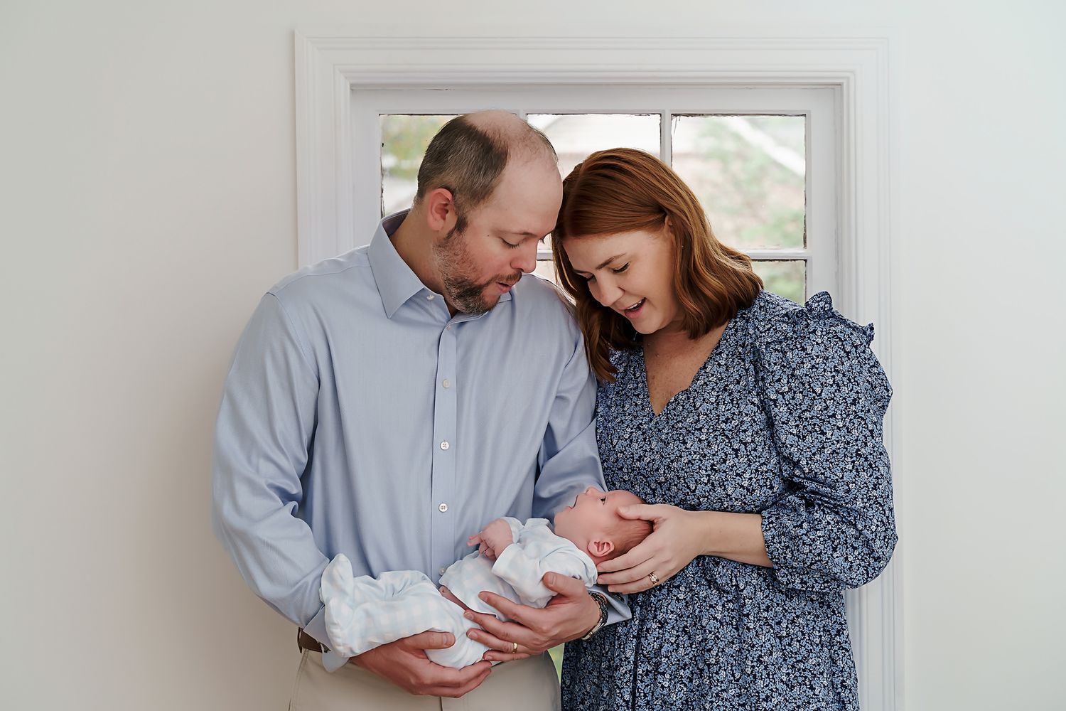 A couple holding their newborn in front of a window during a Forest Acres in-home newborn photography session in Columbia SC.