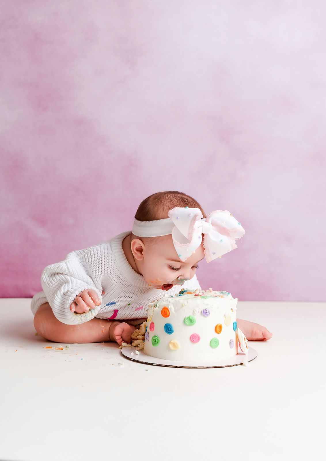 A little girl enjoying her cake in front of a simple pink backdrop during a Studio Cake Smash Session for a client from Newberry SC.