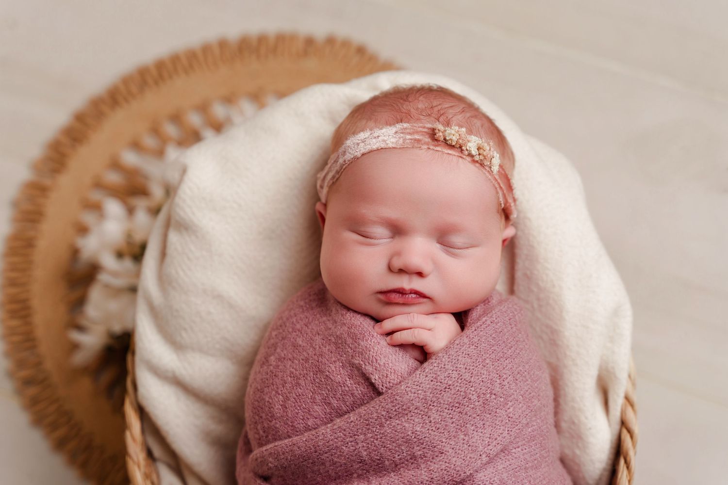 Lexington SC newborn portrait of baby girl in a mauve swaddle in a basket with a cream background and natural wood tones as well.