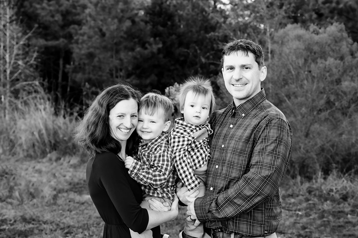 Black and White Family Portrait of Mom and Dad holding their two young boys and grinning at the camera during a Lexington SC Family Session.