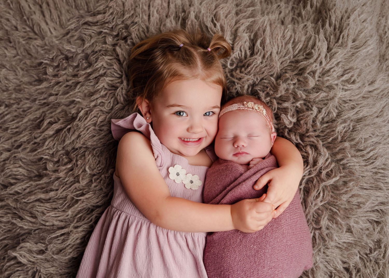Newborn Portrait of a smiling toddler girl snuggling with her new baby sister using soft colors during a Chapin SC Studio Newborn Session.