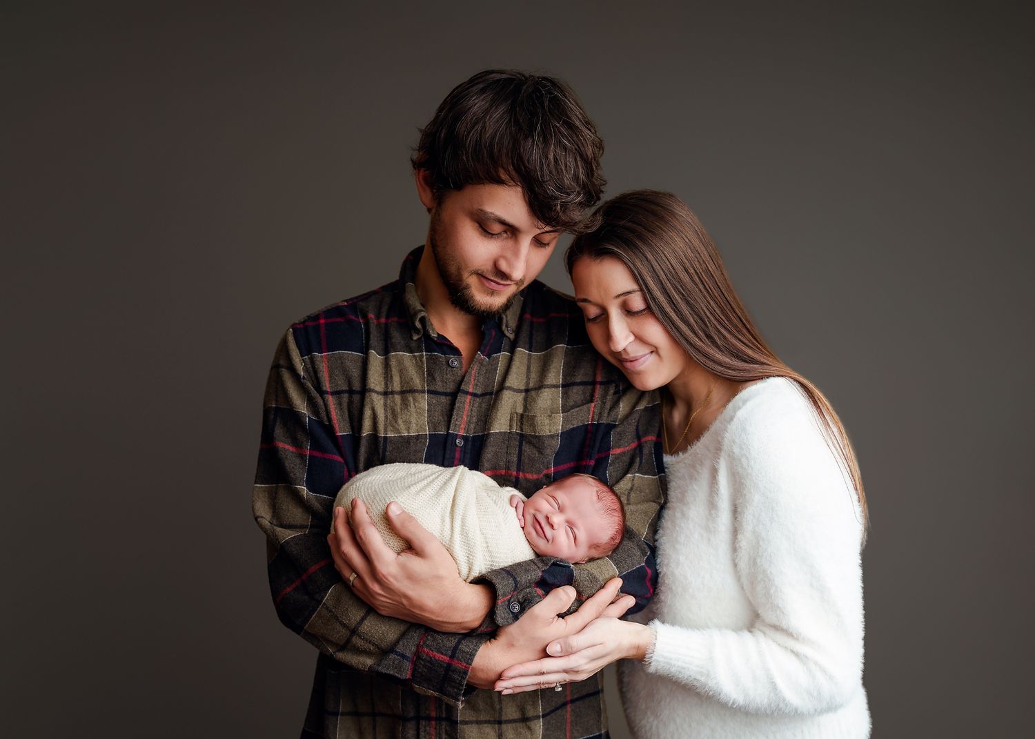 Dad cradling his newborn baby girl as mom leans into him, while both of them look down at her smiling during a Lexington SC Studio Session.