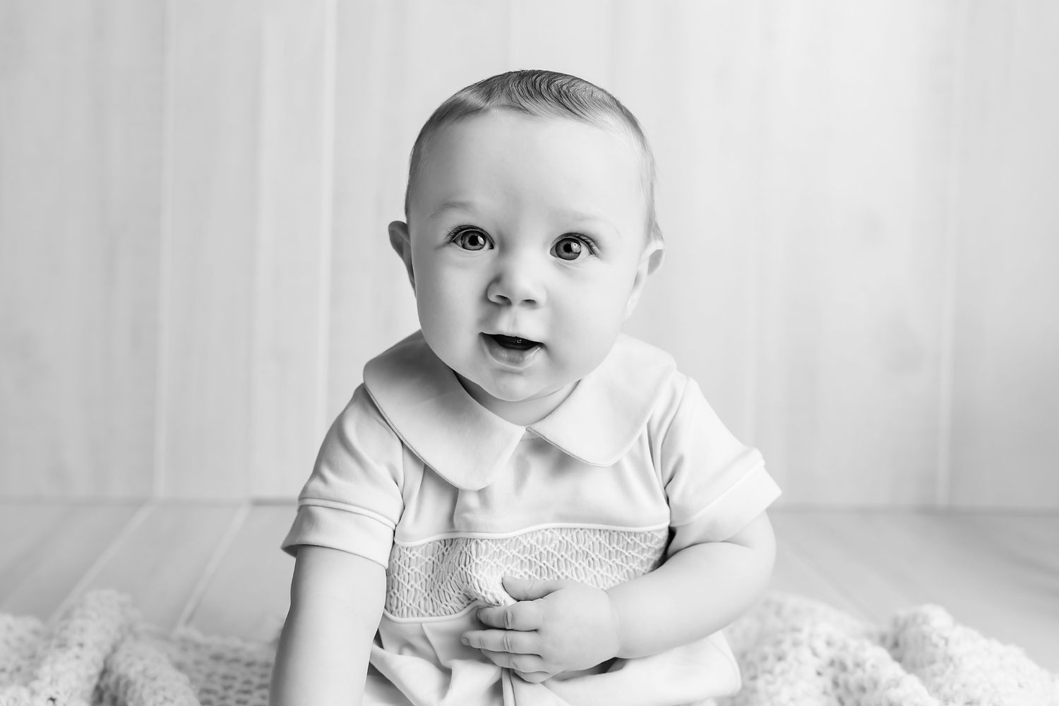 Black and White image of a sweet 6 month old little boy sitting up proudly and grinning at the camera during his 6 Month Portrait Session.