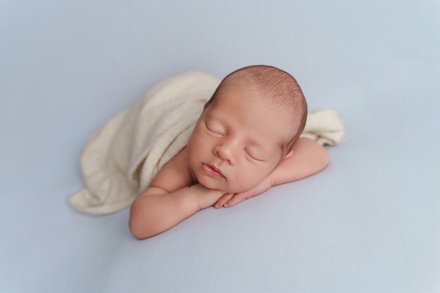 Simple posed image of baby boy on a blue backdrop with a cream wrap accent taken during a studio newborn portrait session in Chapin SC.