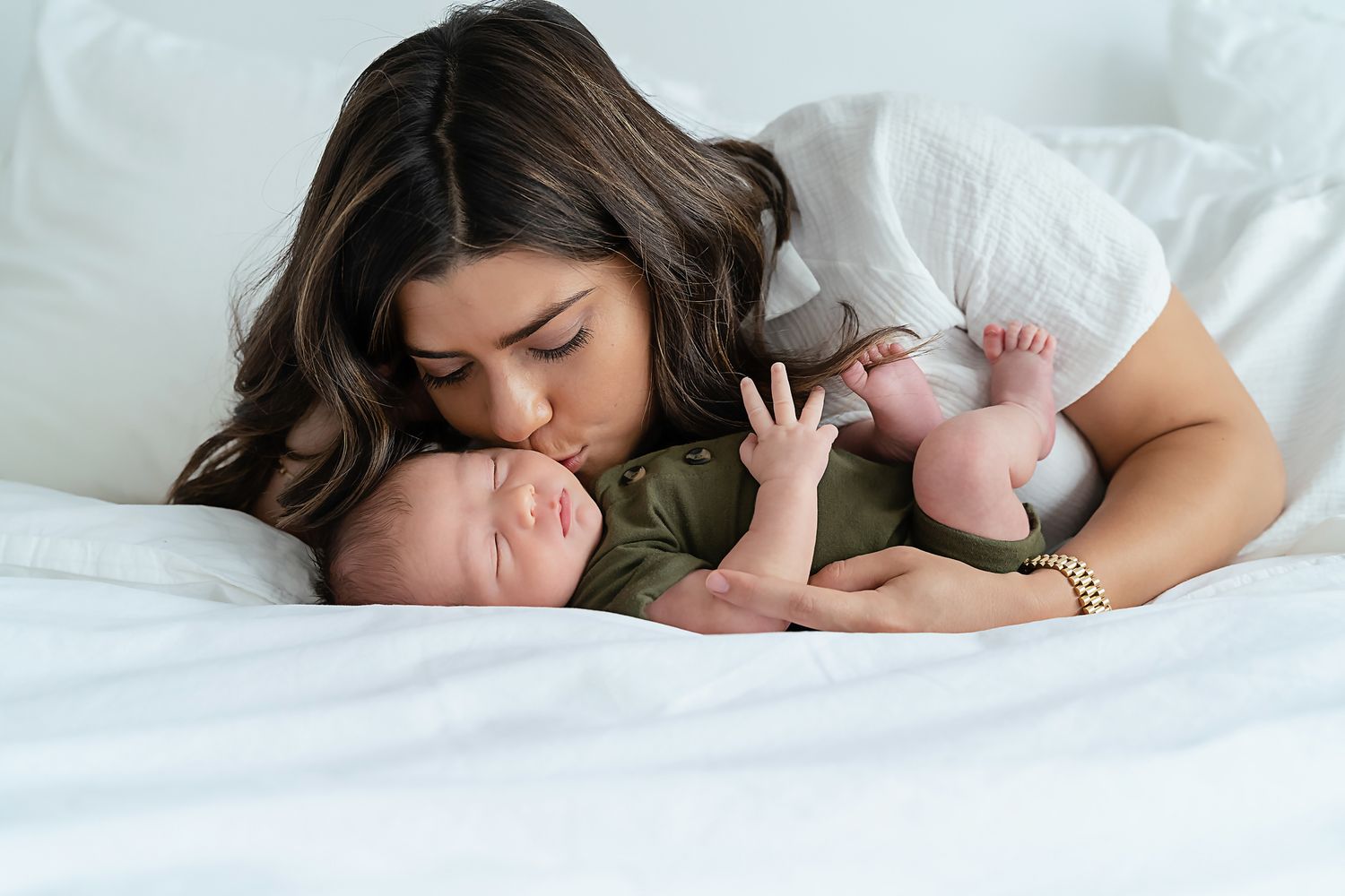 Mom kissing her newborn on the cheek as he stretches out against her during an in-home newborn session in Chapin SC.