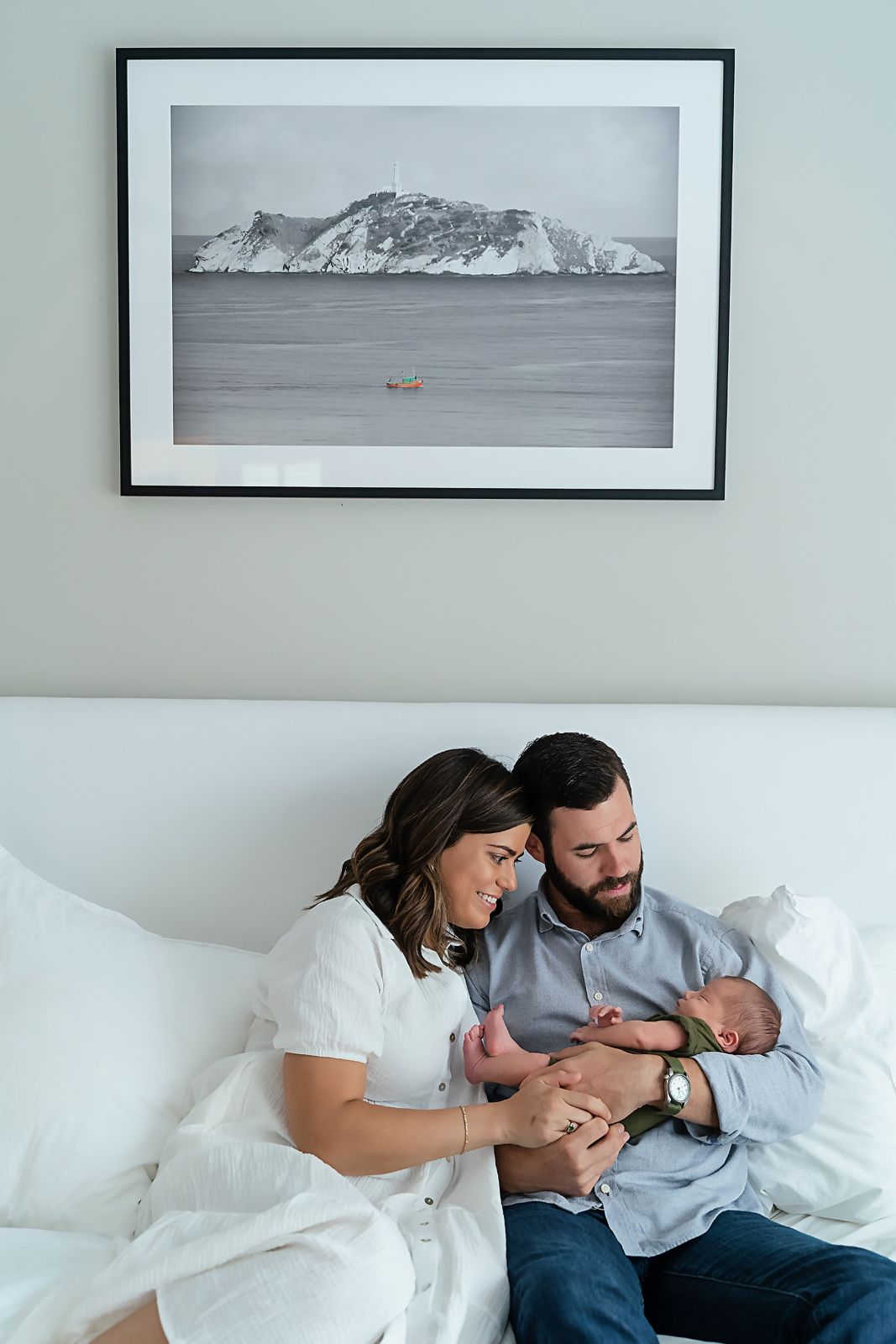 A storytelling shot of parents snuggling their newborn under a piece of artwork in their home during a Chapin SC in-home newborn session.