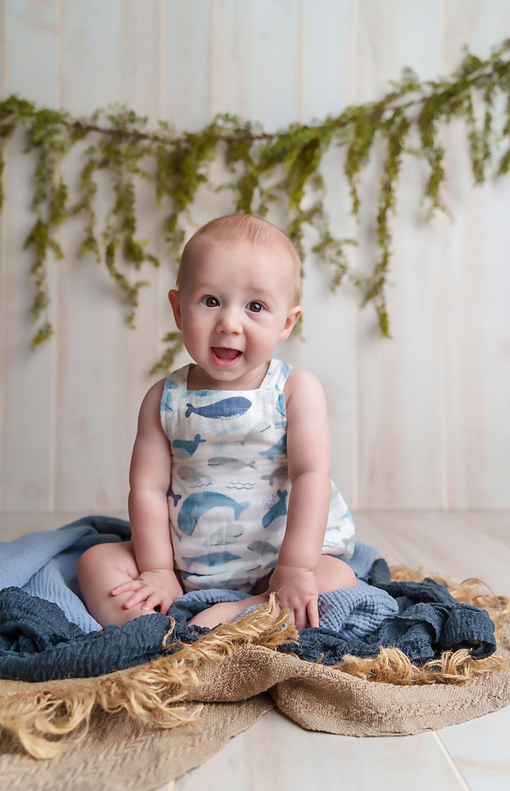 Sweet 6 month old baby boy sitting on blue blankets with a greenery garland behind him during a Lexington SC 6 month milestone session.